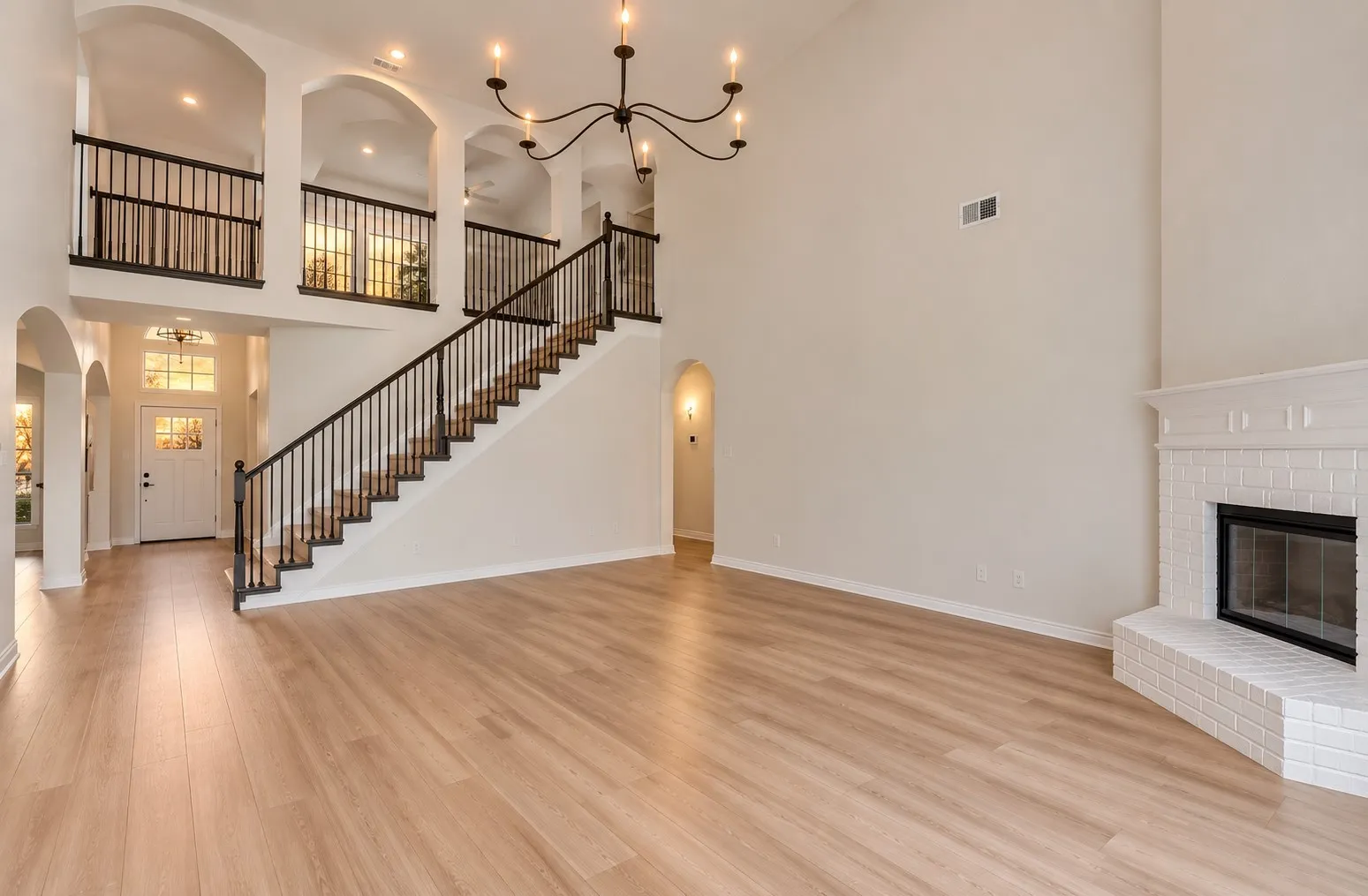 Vaulted ceilings, wood-finish flooring, white brick fireplace, wrought iron balusters, and arched doorways