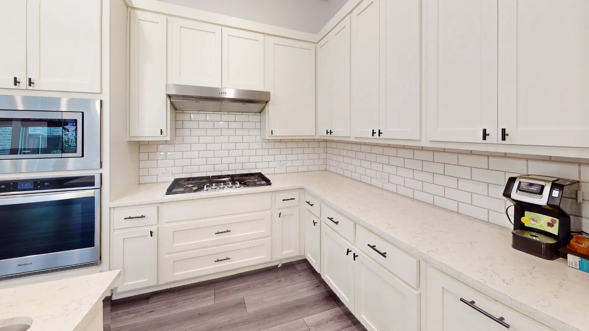 White shaker cabinetry with matte black hardware, stainless steel built-in microwave and oven, gas cooktop, white subway tile backsplash, and light-toned countertops