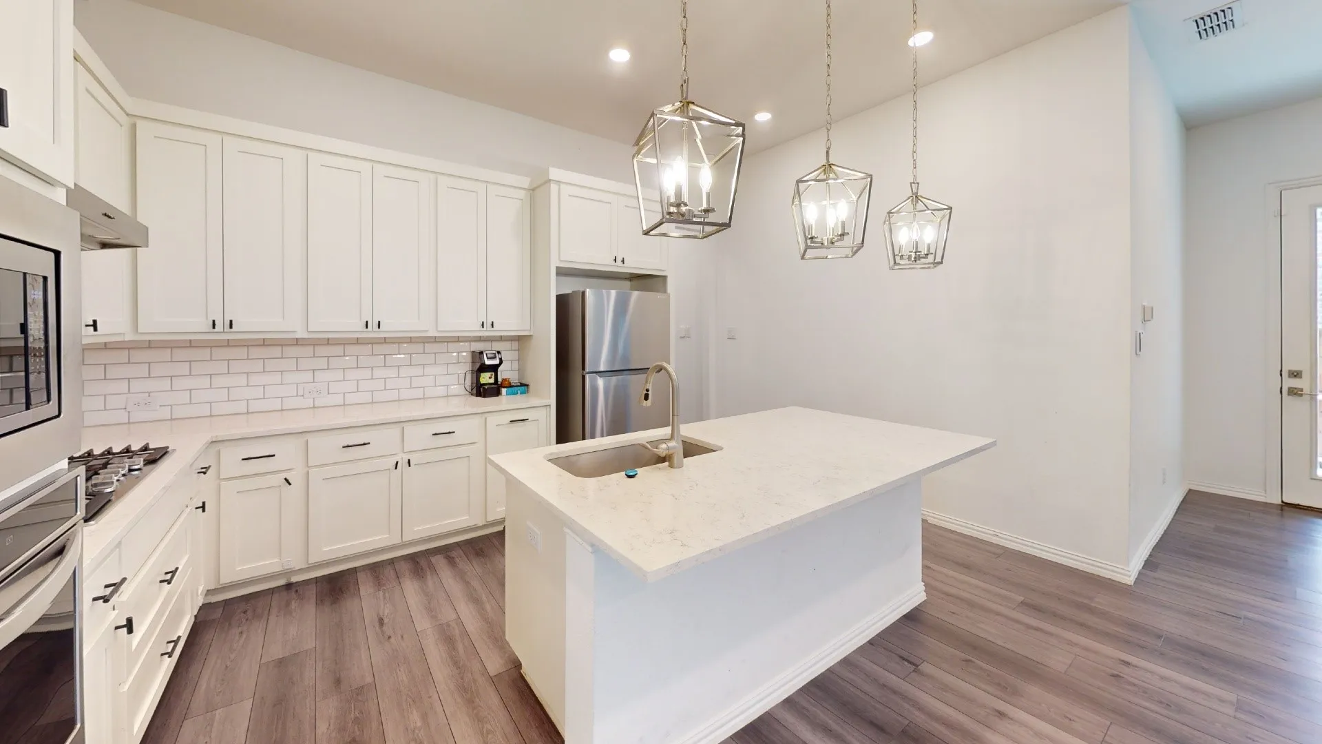 Kitchen featuring white cabinetry, subway tile backsplash, stainless steel appliances, wood-finish flooring, and a center island with pendant lighting