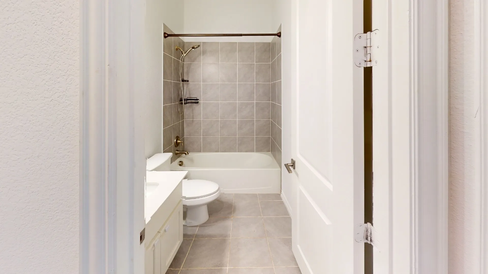 Bathroom featuring a white vanity with an integrated sink, ceramic floor tiling, and a tub with tiled surround