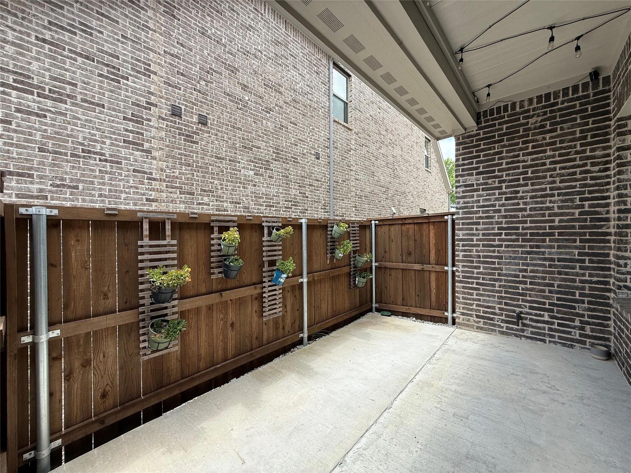 Patio featuring a concrete surface, wood fence, and string lighting