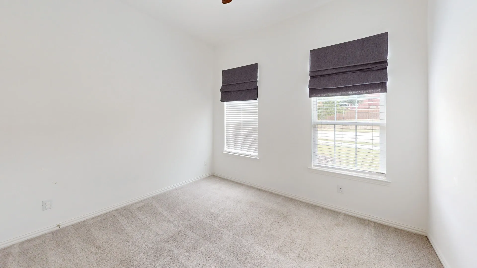 Neutral tone walls, ceiling-mounted light fixture, light-toned carpet flooring, and two windows with blinds and fabric shades