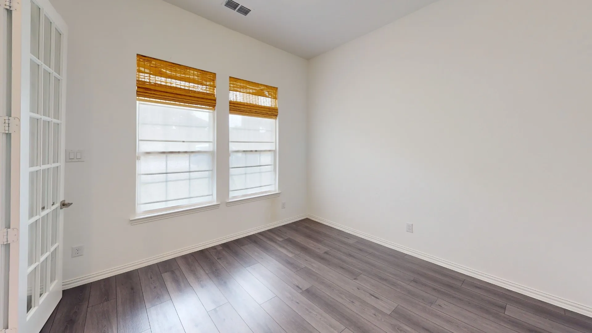 Wood-finish flooring, white walls, and two large windows with horizontal blinds