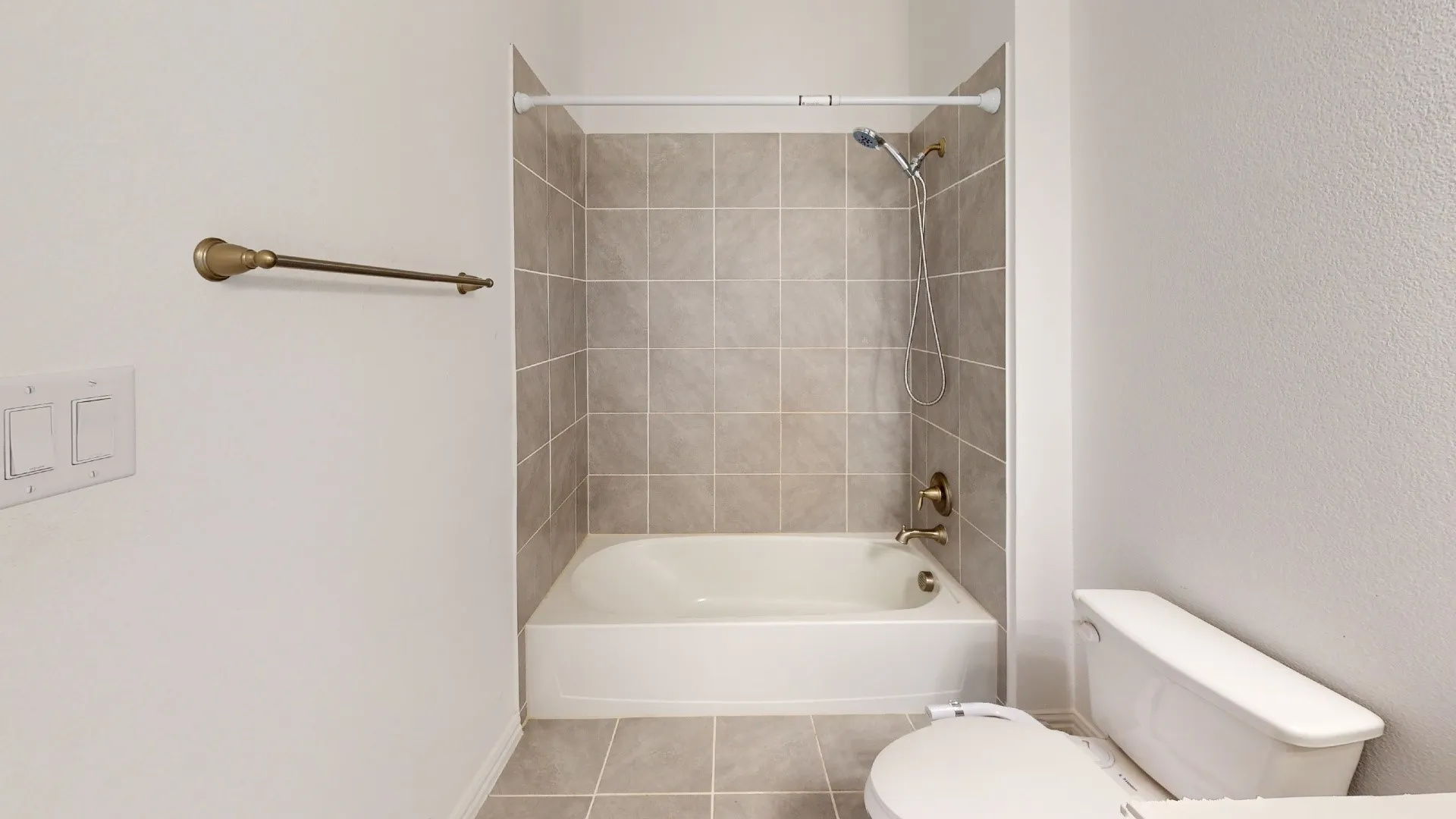 Bathtub with a tiled surround, overhead shower, and adjacent commode