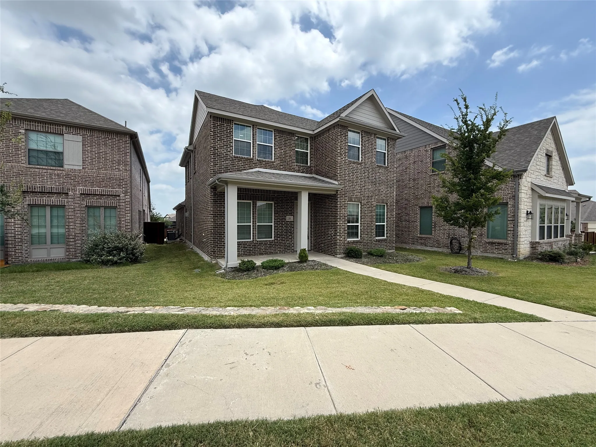 Two-story brick exterior with a covered entry, mature tree, and concrete pathway