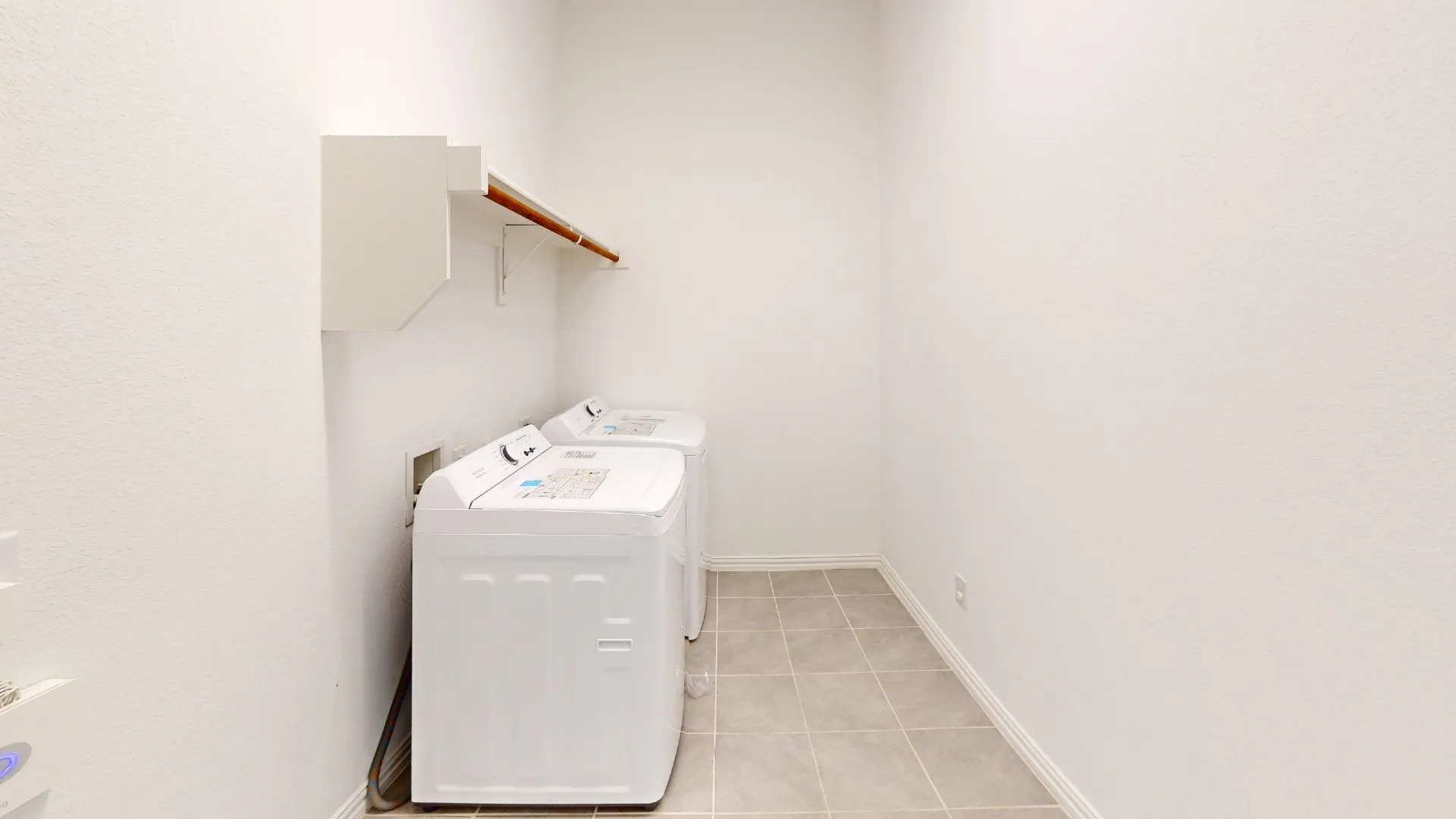 Dedicated laundry area featuring a wall-mounted cabinet, wooden hanging rod, and tiled flooring