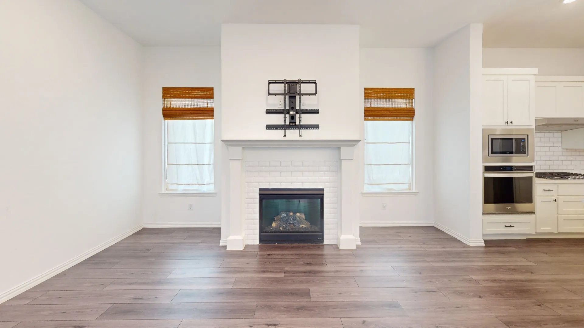 Hardwood-finish flooring throughout, featuring a fireplace with white subway tile surround and mantle, and built-in stainless steel oven and microwave