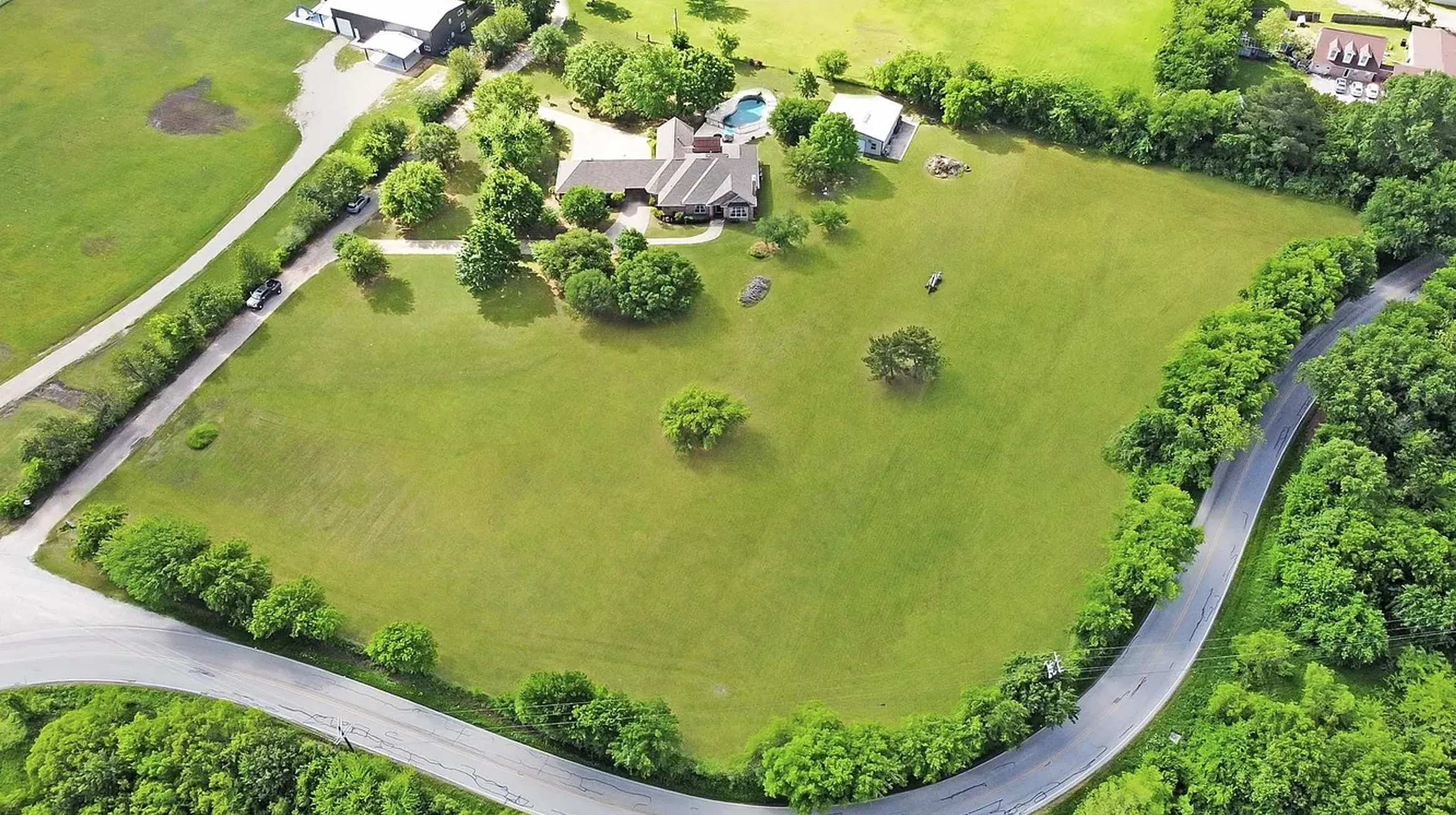 Expansive green space with mature trees, a private residence, and an in-ground pool
