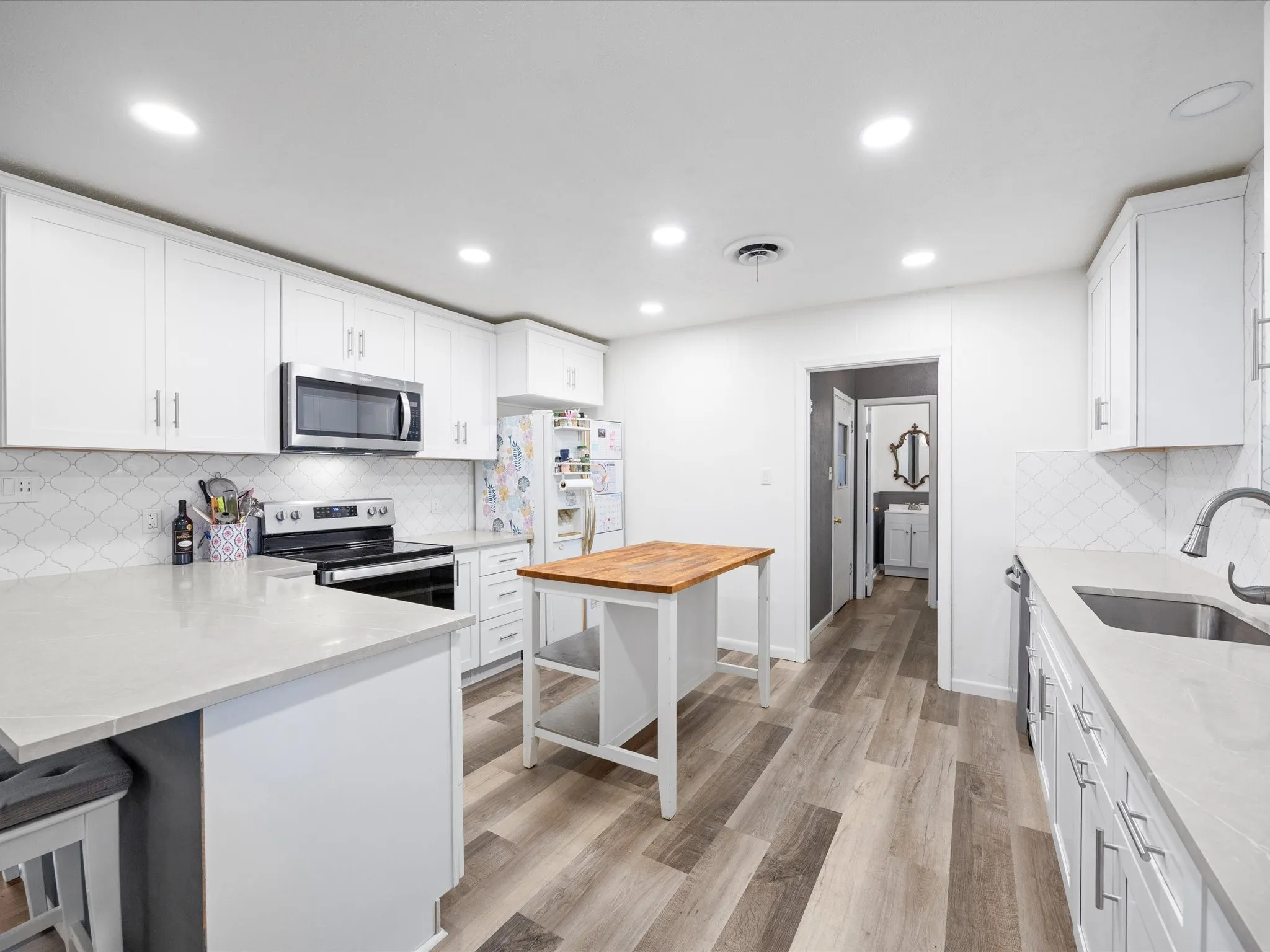 Contemporary kitchen featuring white cabinetry, light-toned countertops, stainless steel appliances, wood-finish flooring, and a freestanding island with a butcher block top