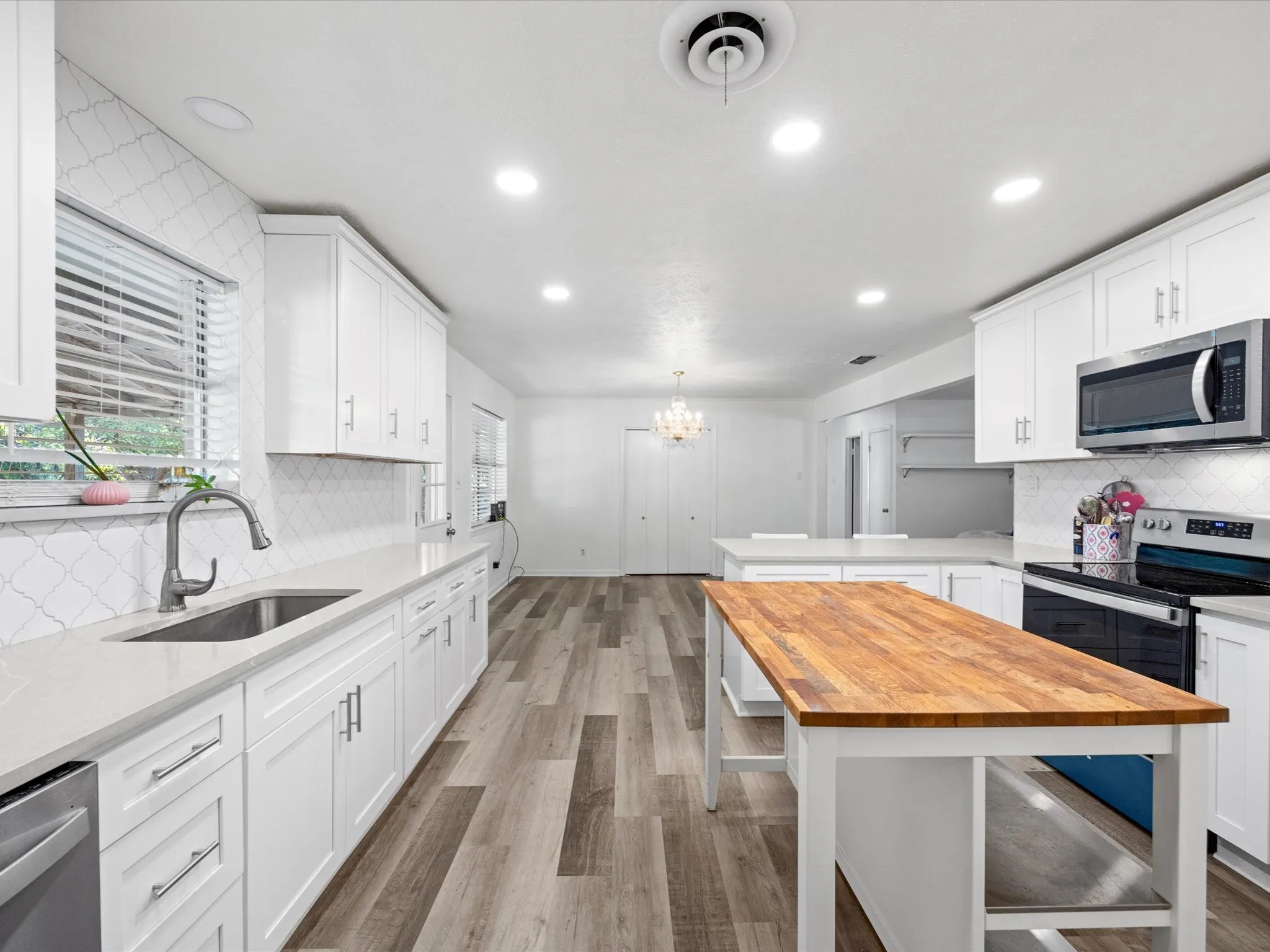 White cabinetry with stainless steel hardware, wood-finish flooring, white solid surface countertops, stainless steel appliances, and a wood-top kitchen island