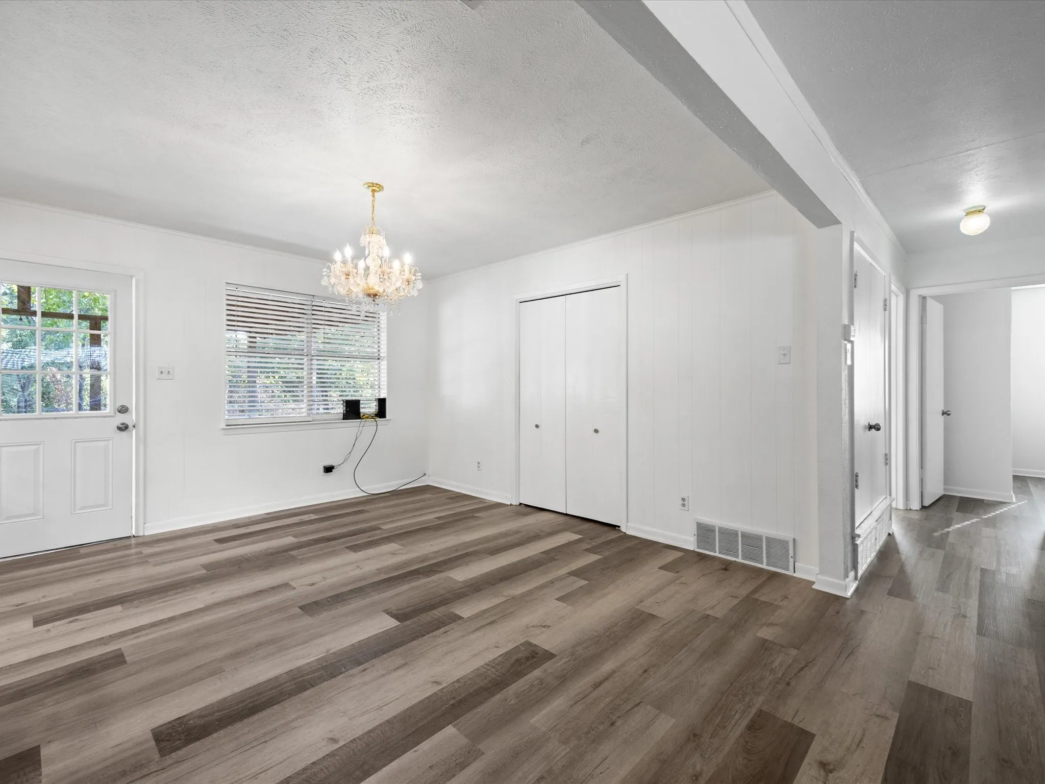 Wood-finish flooring, white walls, and a multi-tiered chandelier