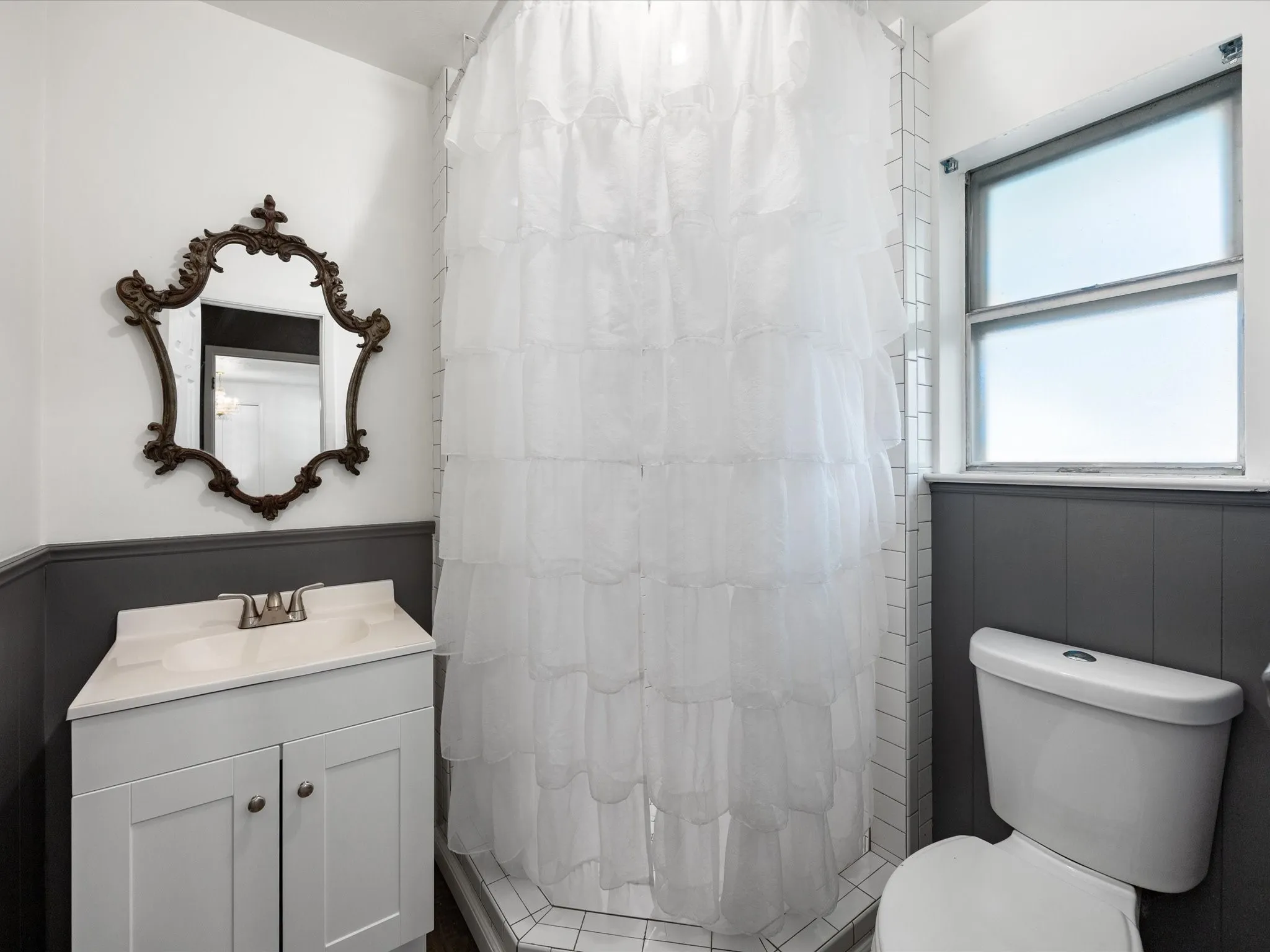 White paneled vanity with integrated sink, brushed nickel faucet, and a decorative framed mirror