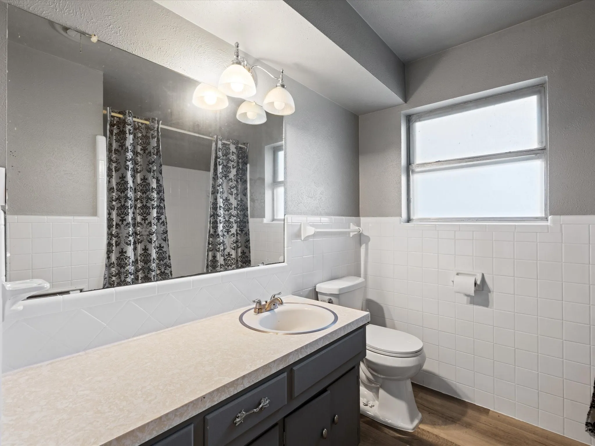 Bathroom featuring a vanity with an integrated sink, a large wall-mounted mirror, white square tile wainscoting, and wood-finish flooring