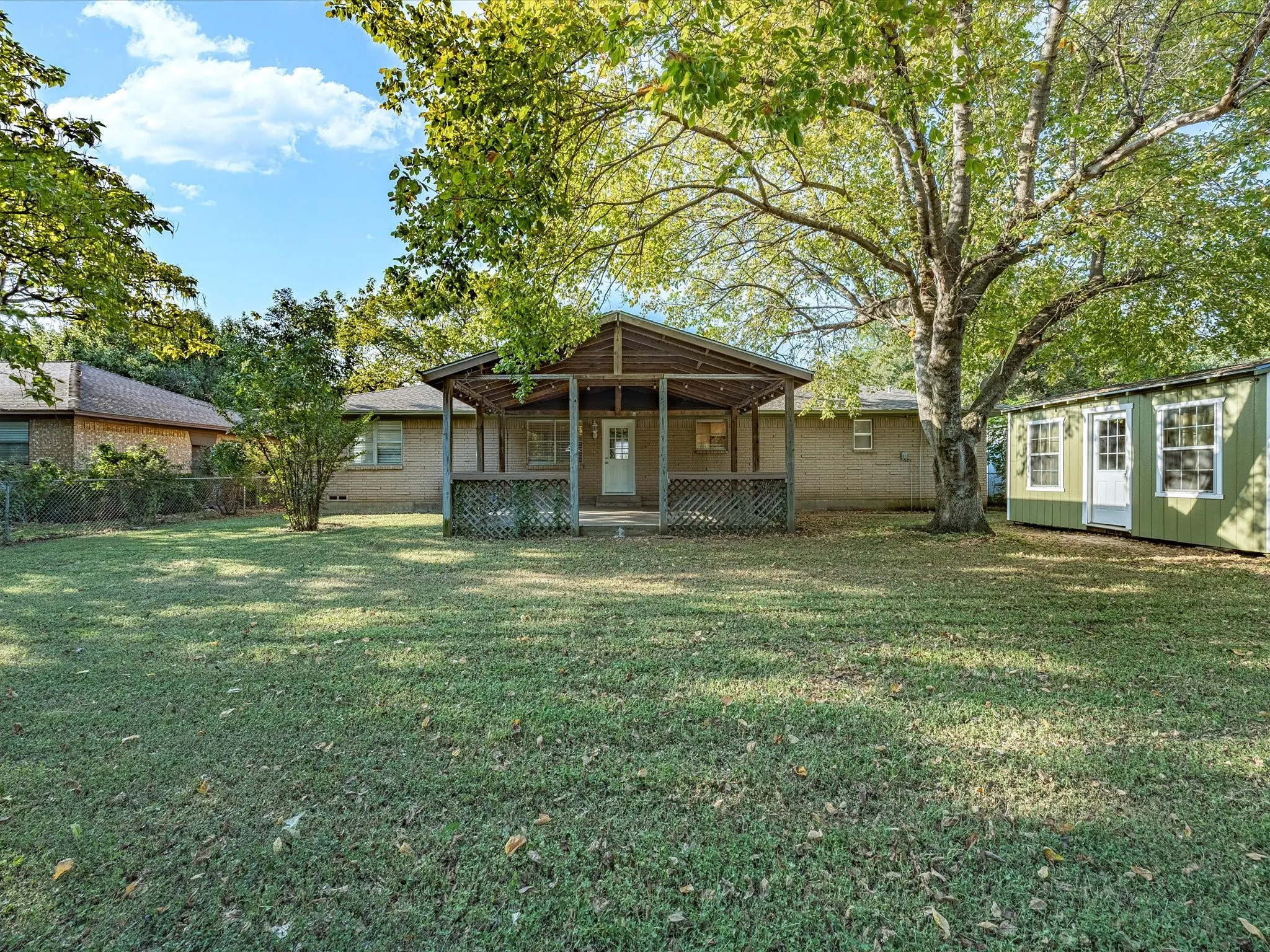 Expansive backyard with a covered patio, mature trees, and a detached storage shed