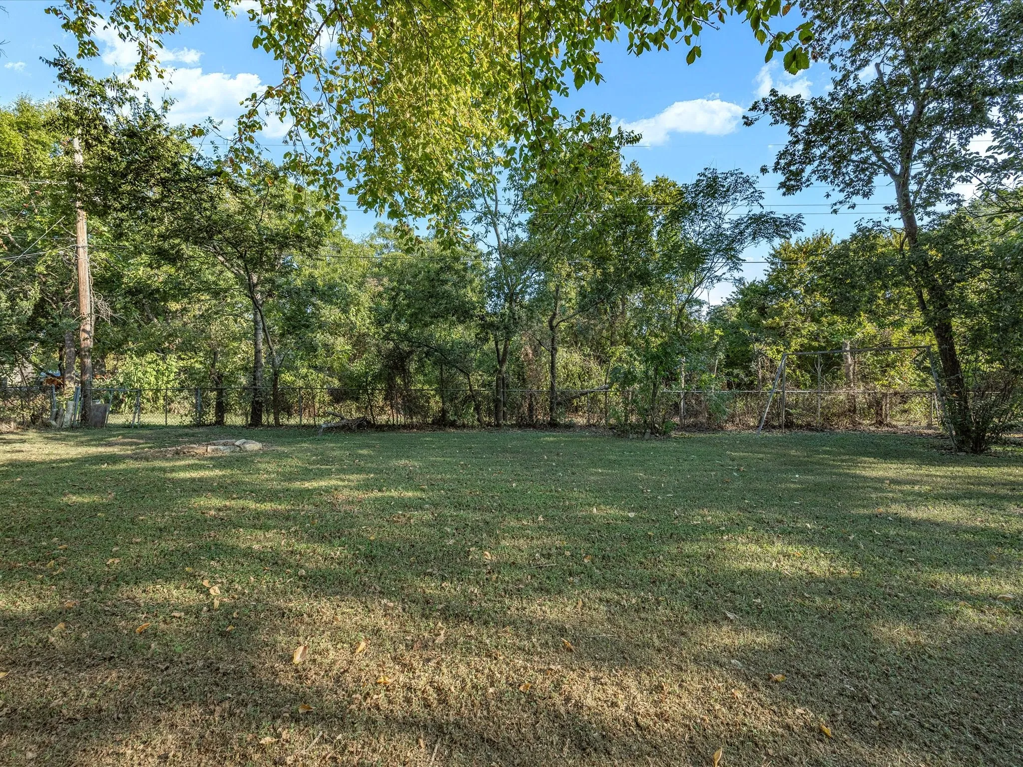 Expansive green lawn with mature trees and a chain-link fence
