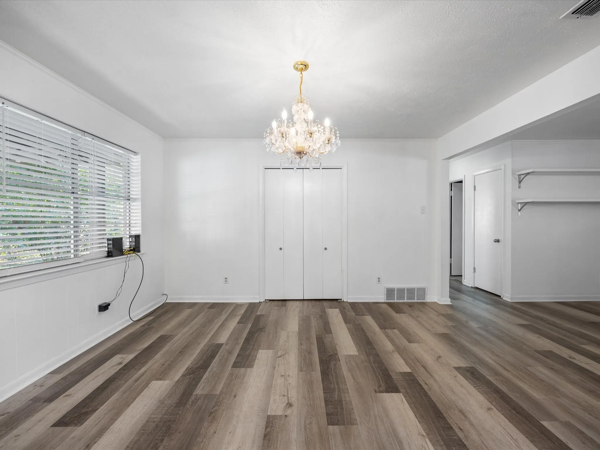 Wood-finish flooring throughout, bright white walls, and a crystal chandelier
