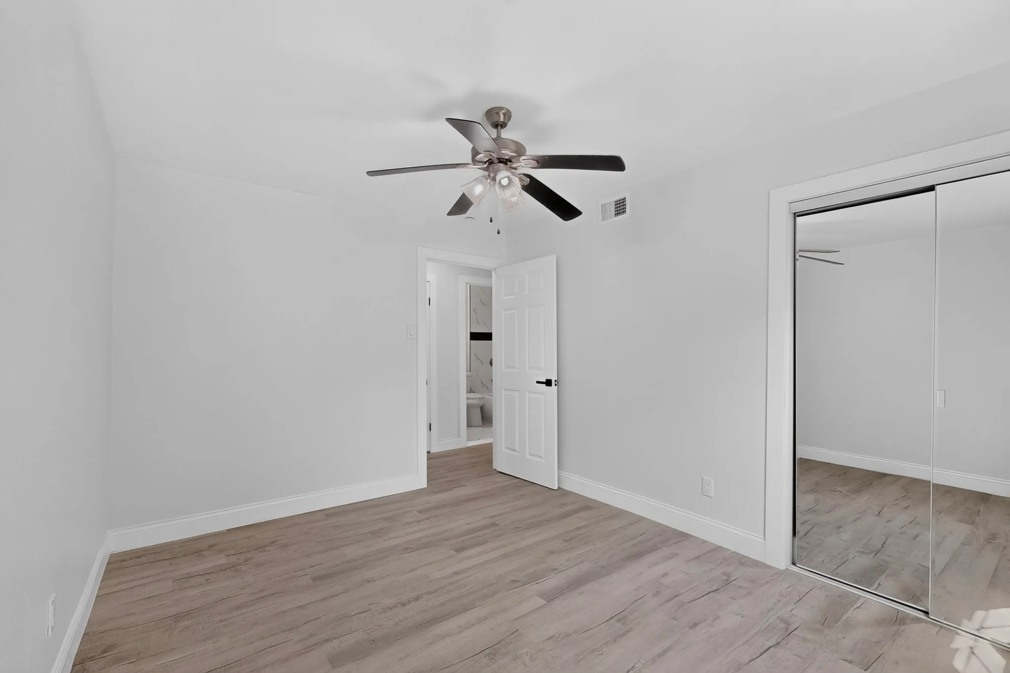 Spacious room featuring wood-finish flooring, a ceiling fan with integrated lighting, and mirrored closet doors