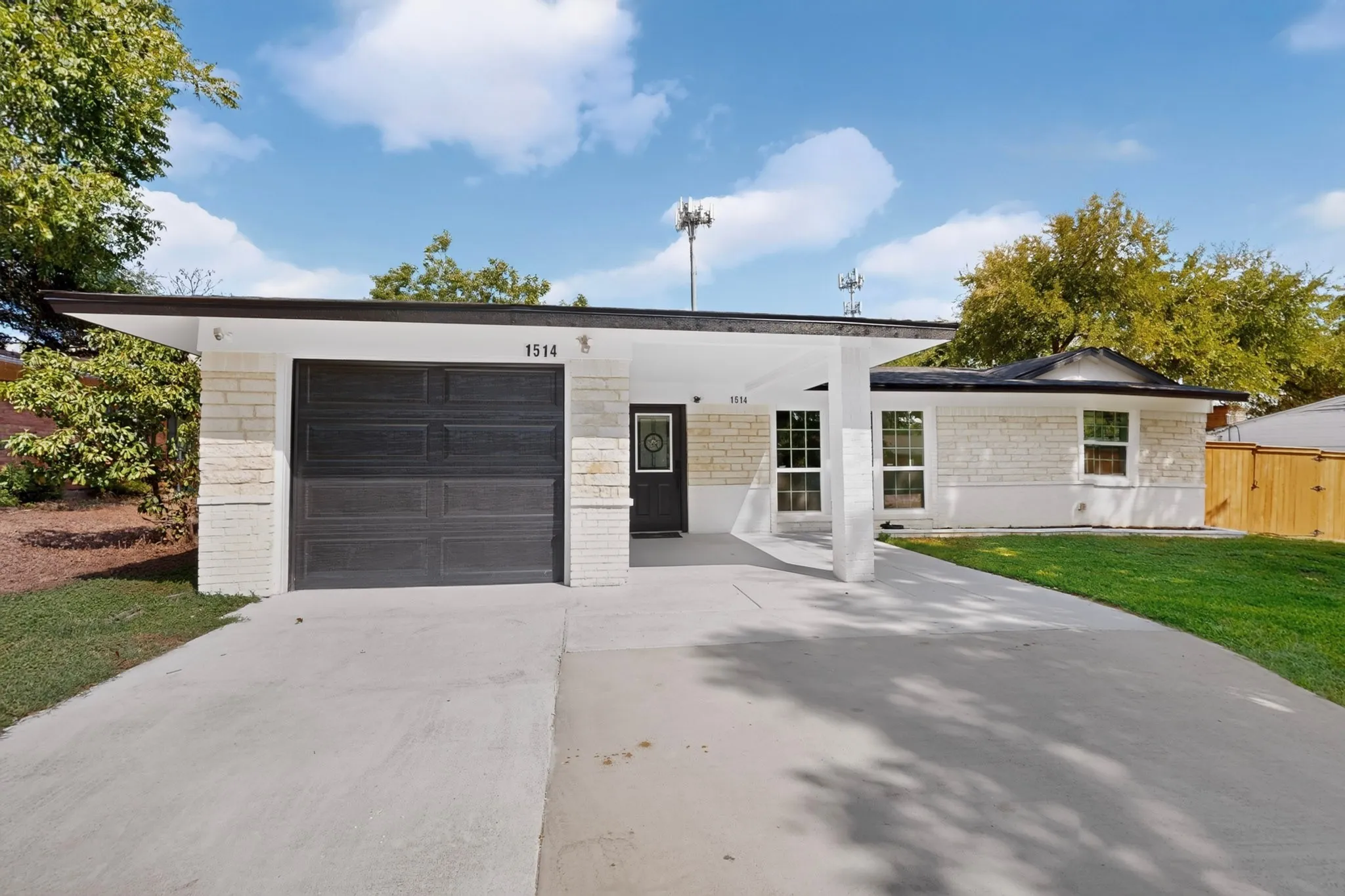 White brick exterior with a black roof, attached carport, concrete driveway, and an integrated garage
