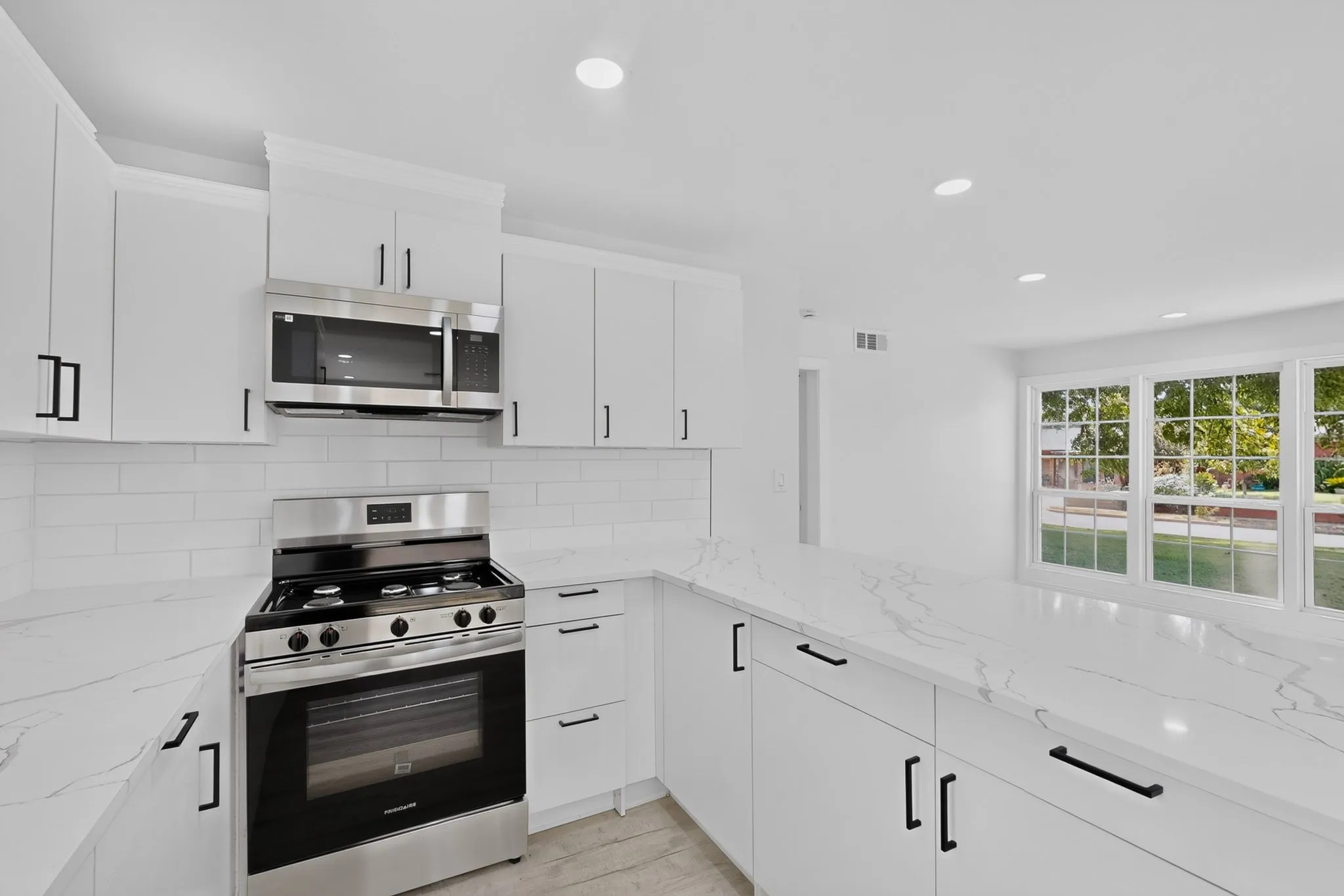 White cabinetry with black hardware, stainless steel appliances, white subway tile backsplash, white countertops, and recessed lighting