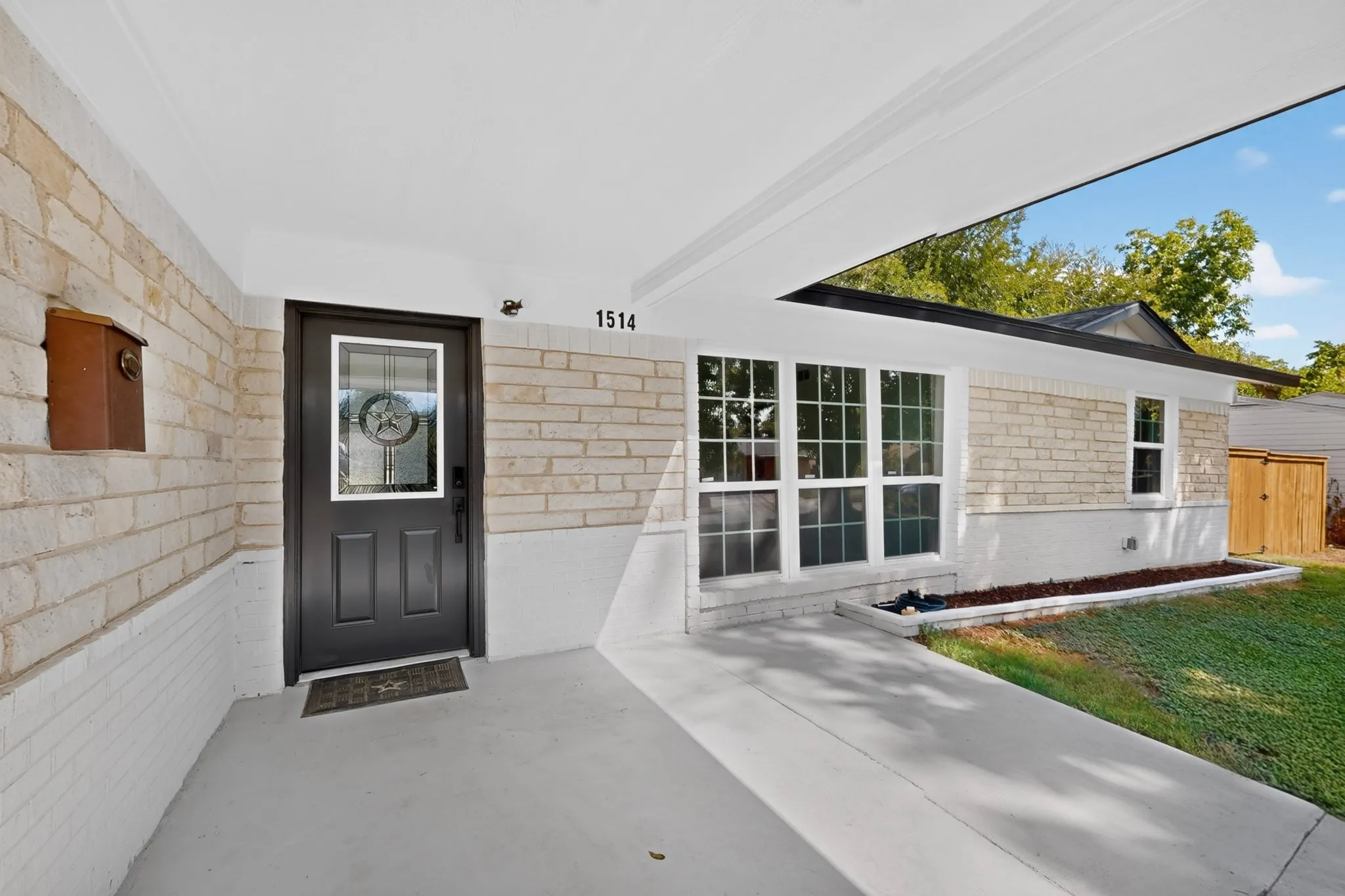 Light-colored brick exterior with white trim, covered concrete entry, dark paneled front door with decorative glass insert, and multi-pane windows