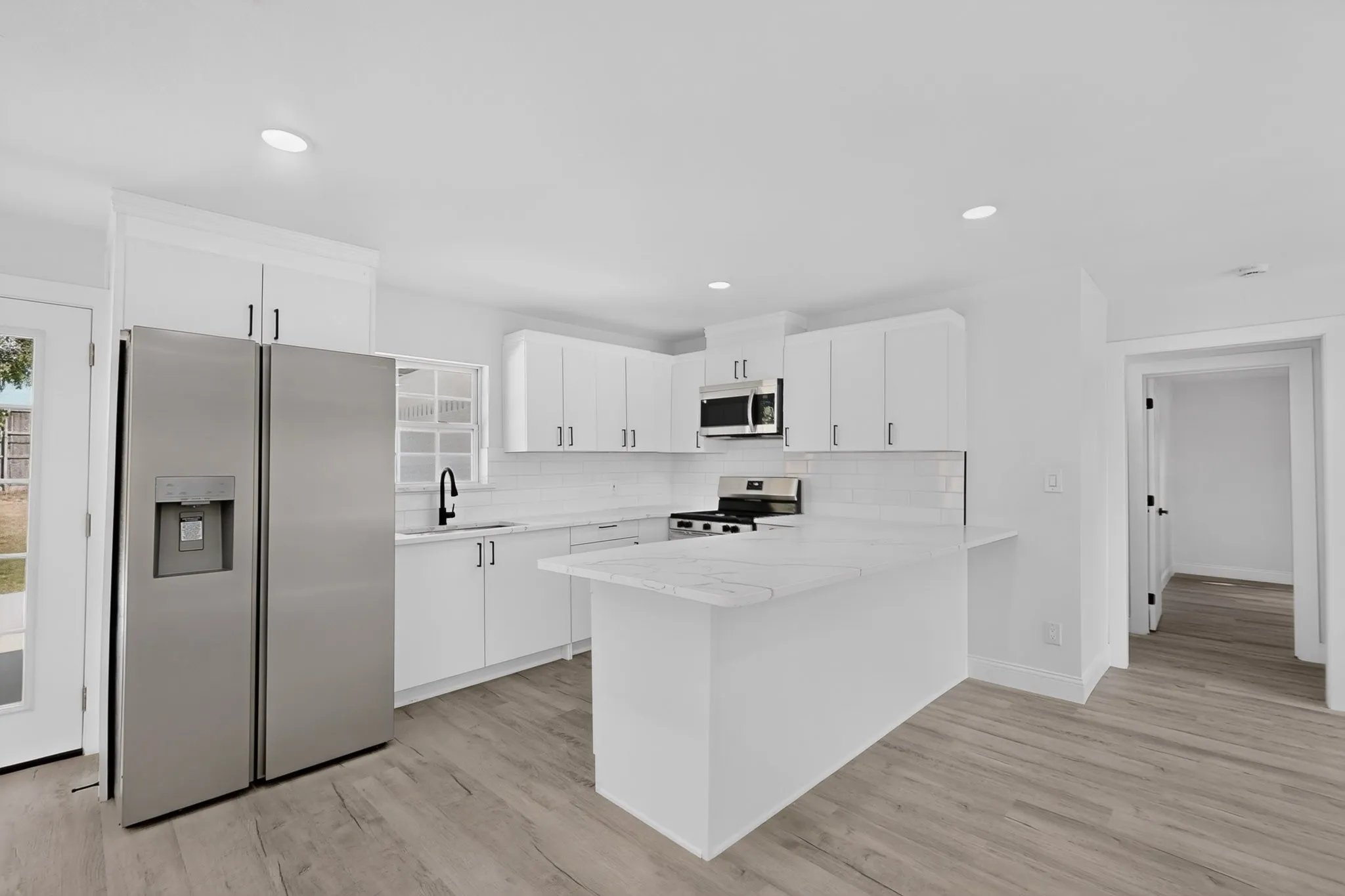Kitchen featuring white cabinetry, stainless steel appliances, a white subway tile backsplash, and vinyl wood-finish flooring