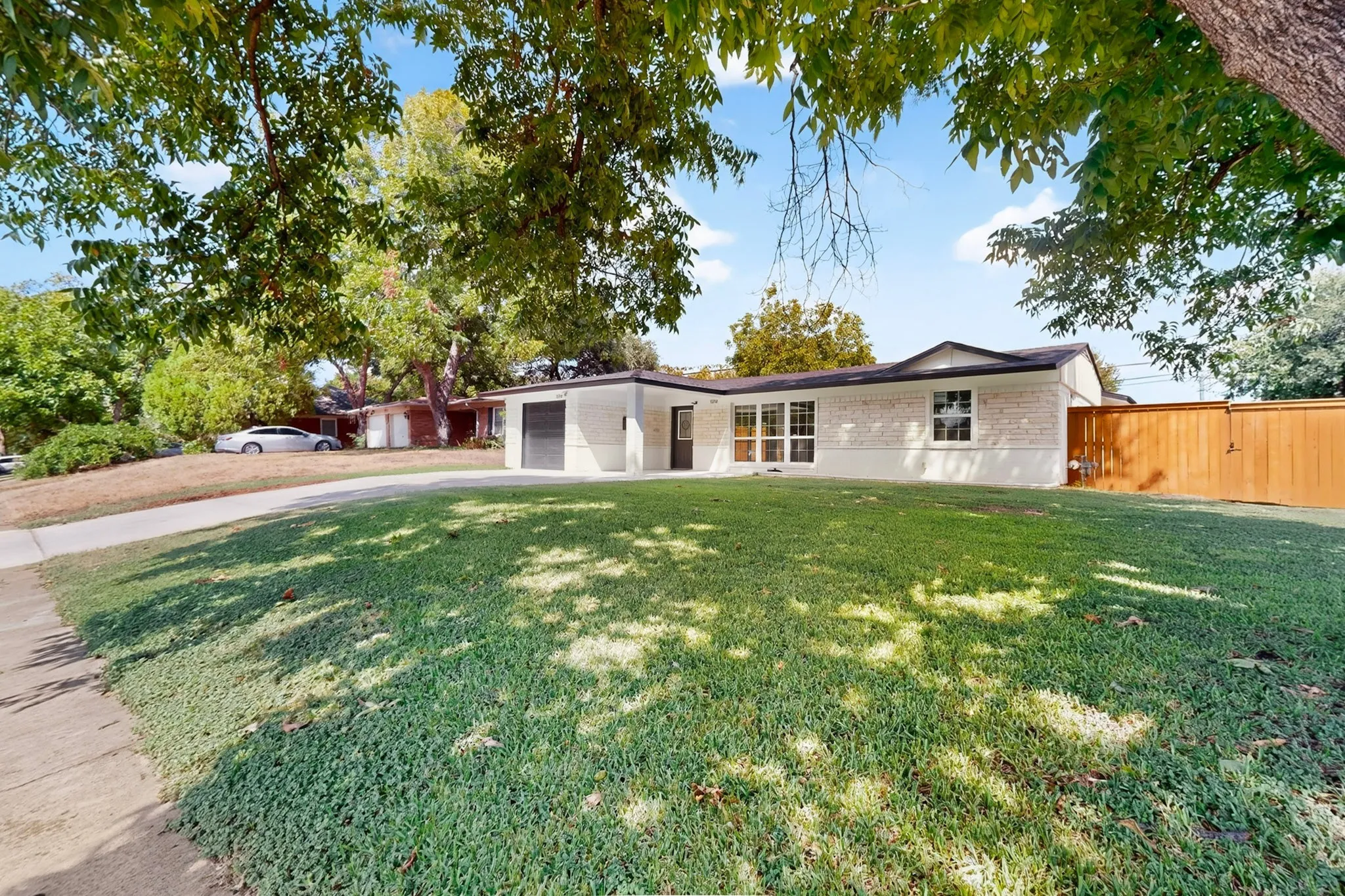 White brick exterior with black trim, integrated garage, front lawn with established landscaping, and a wooden fence