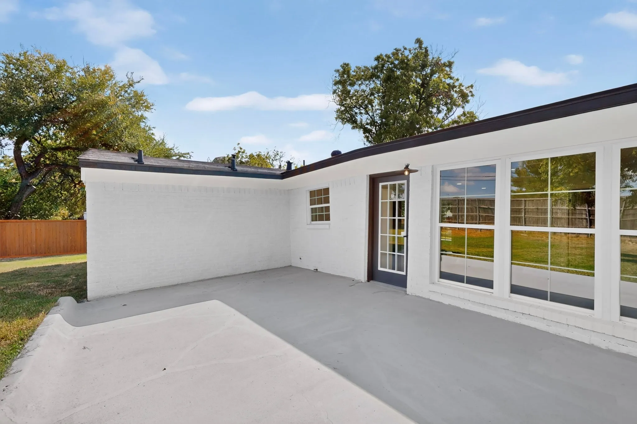 Rear exterior featuring a concrete patio, white painted brick, and large windows