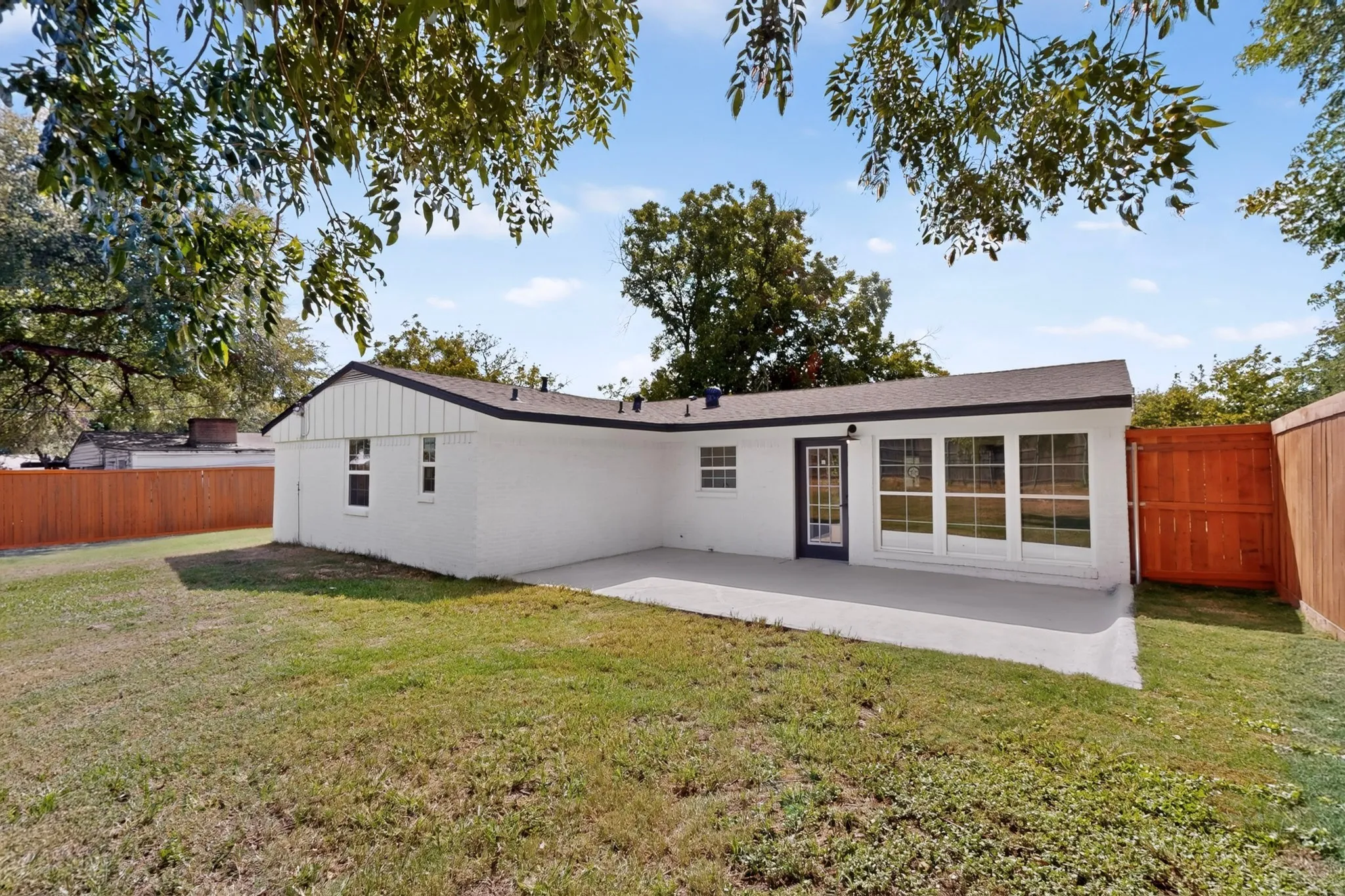 Expansive backyard featuring a white painted brick exterior, a paved patio, a rear entry door, and a row of large windows