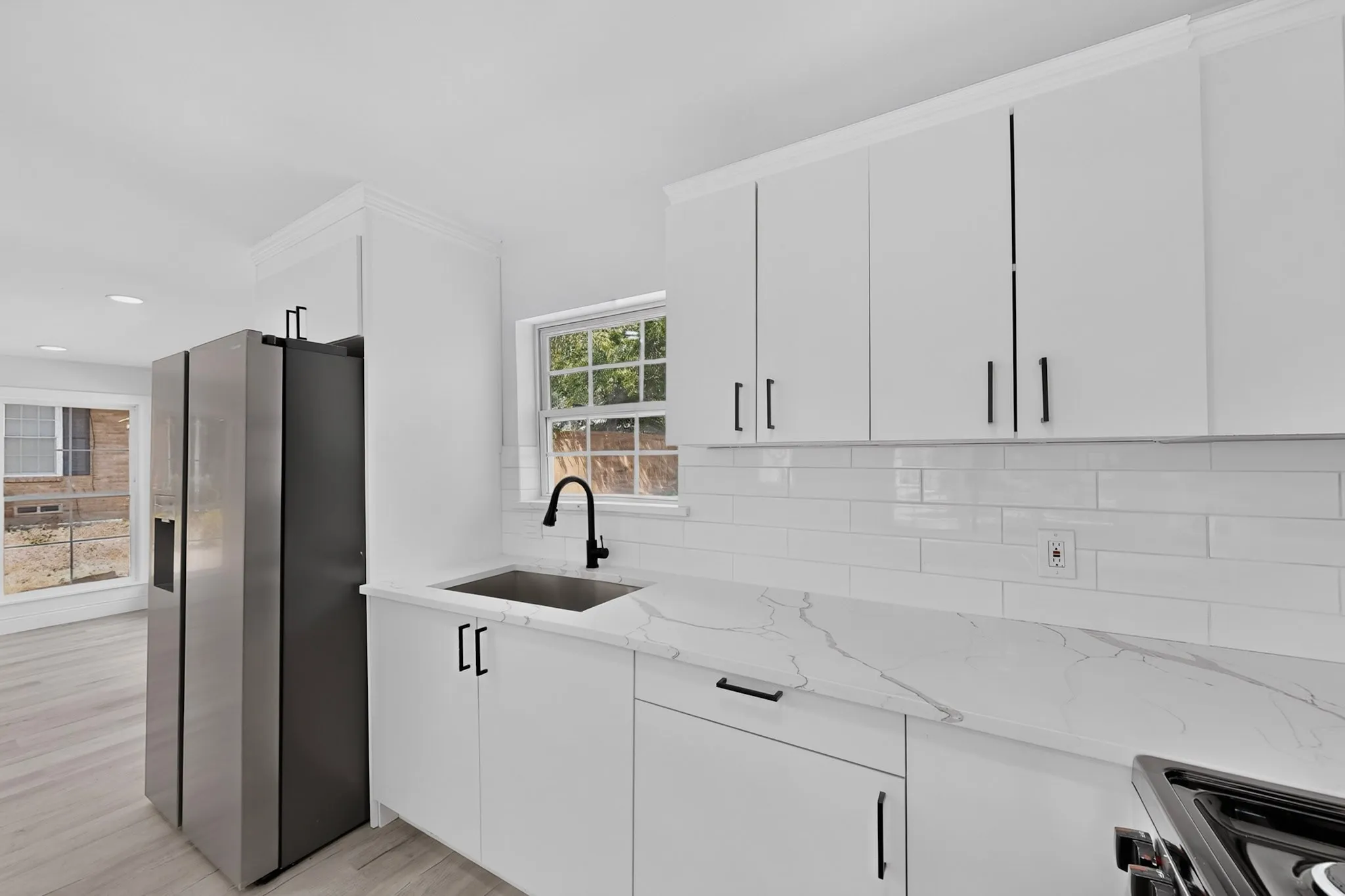 Modern kitchen featuring white shaker-style cabinetry, white subway tile backsplash, and light-toned wood-finish flooring