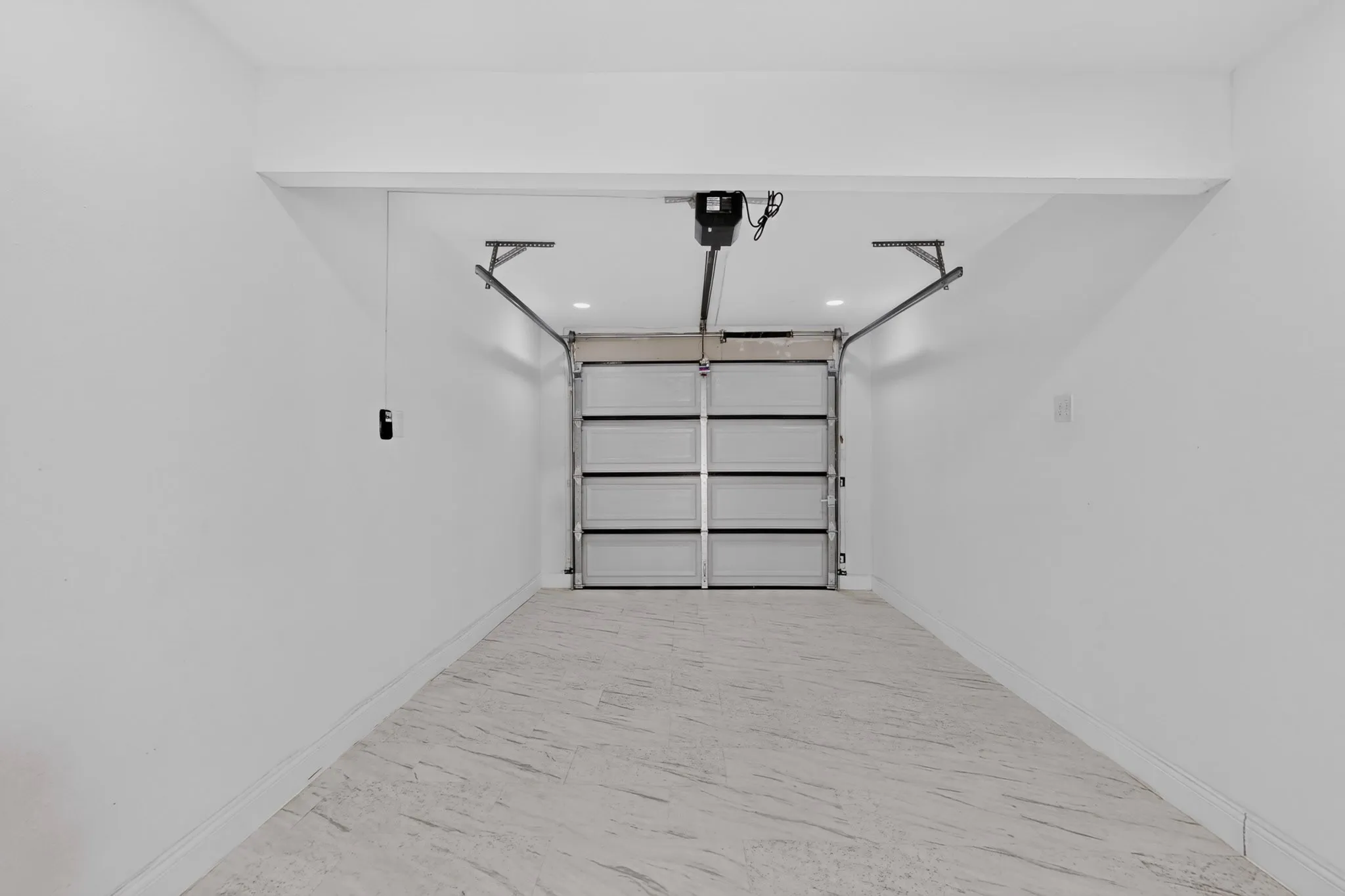 Spacious garage with a modern sectional garage door, automatic opener, and light-toned tile flooring