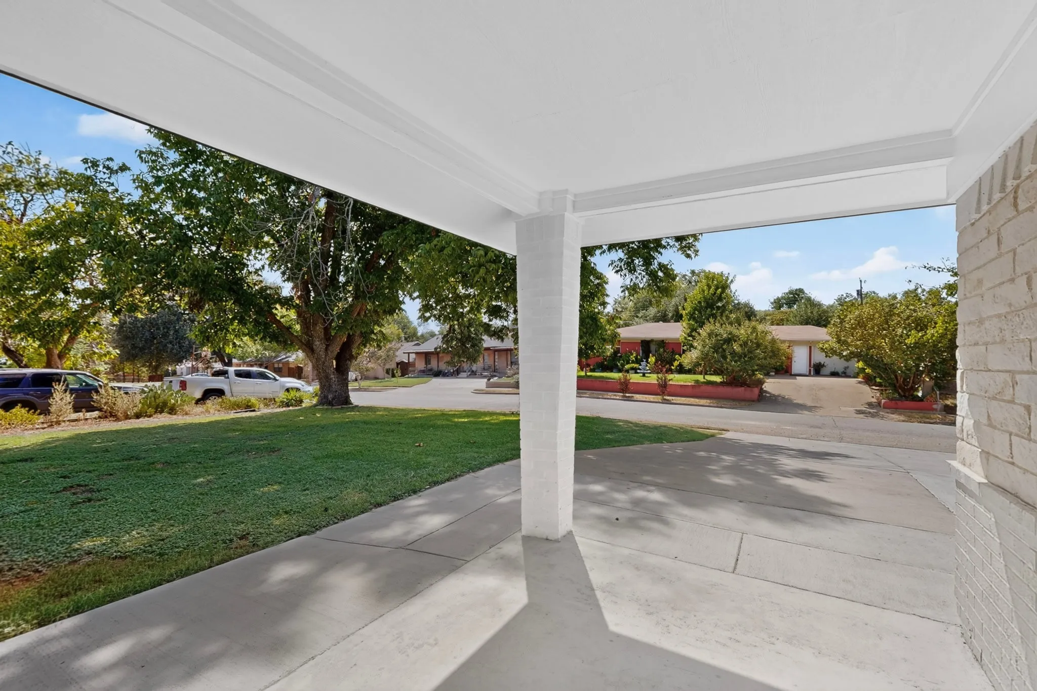 Covered concrete porch with white support columns and a white brick exterior