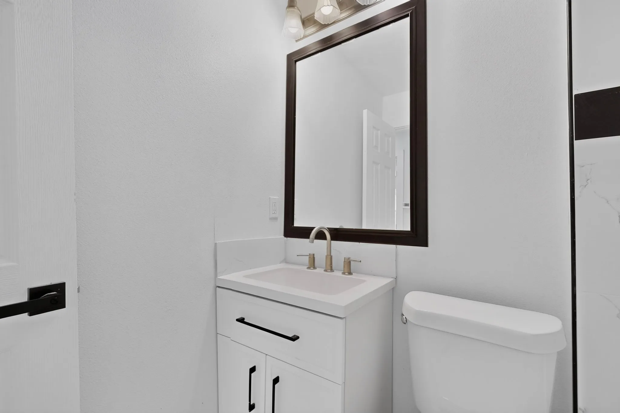 White vanity with a white countertop and integrated sink, framed mirror, and chrome-finish faucet