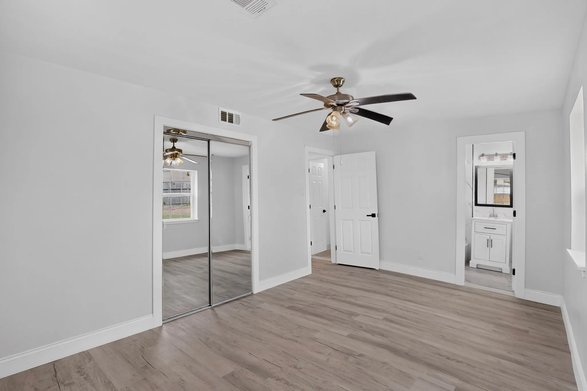 Wood-finish flooring, mirrored closet doors, ceiling fan with light fixture, and white interior doors with black hardware