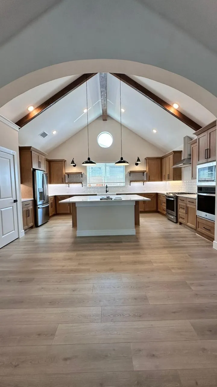 Vaulted ceiling with exposed beams, wood-finish flooring, central island, stainless steel appliances, and shaker-style cabinetry