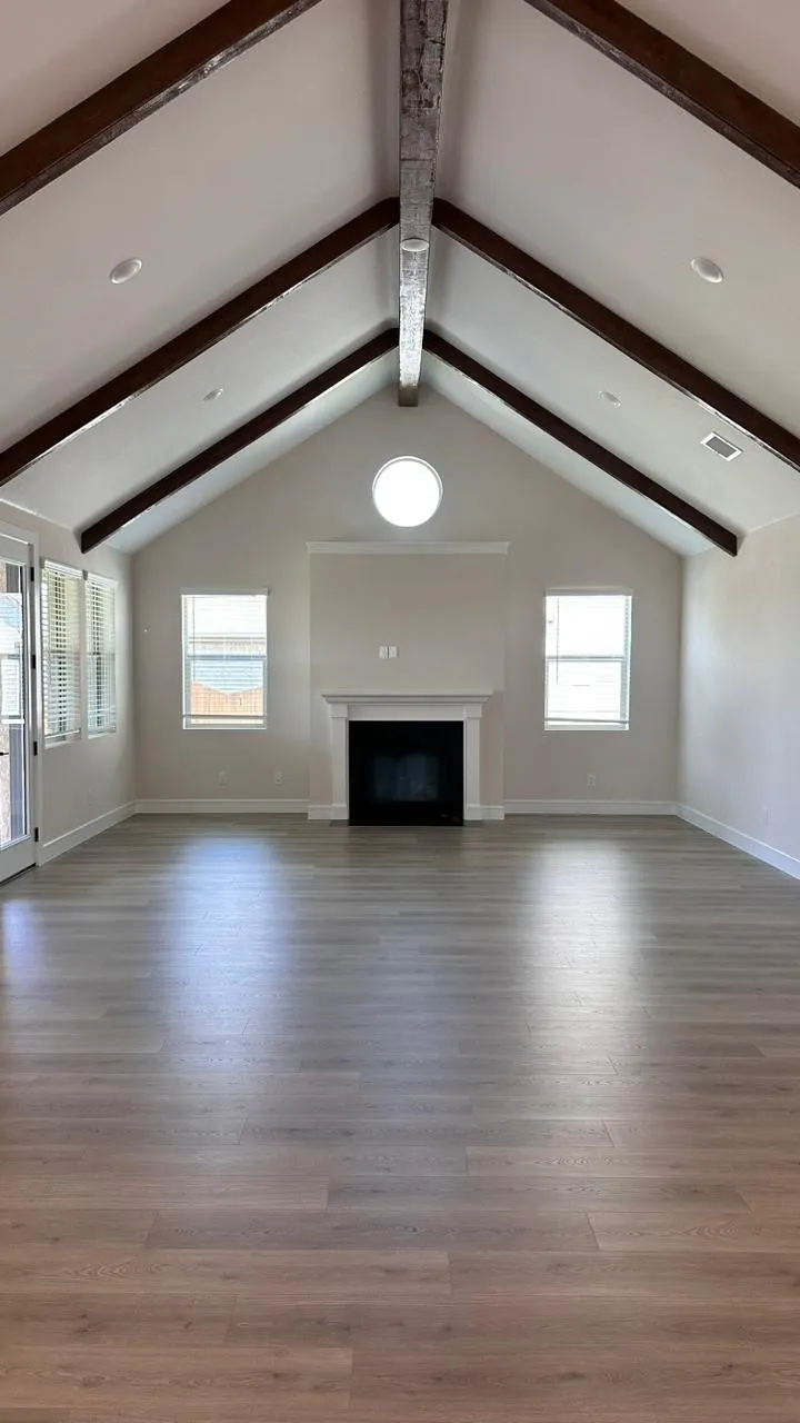 Vaulted ceiling with exposed wood beams, recessed lighting, fireplace with mantel, wood-finish flooring, and a round accent window