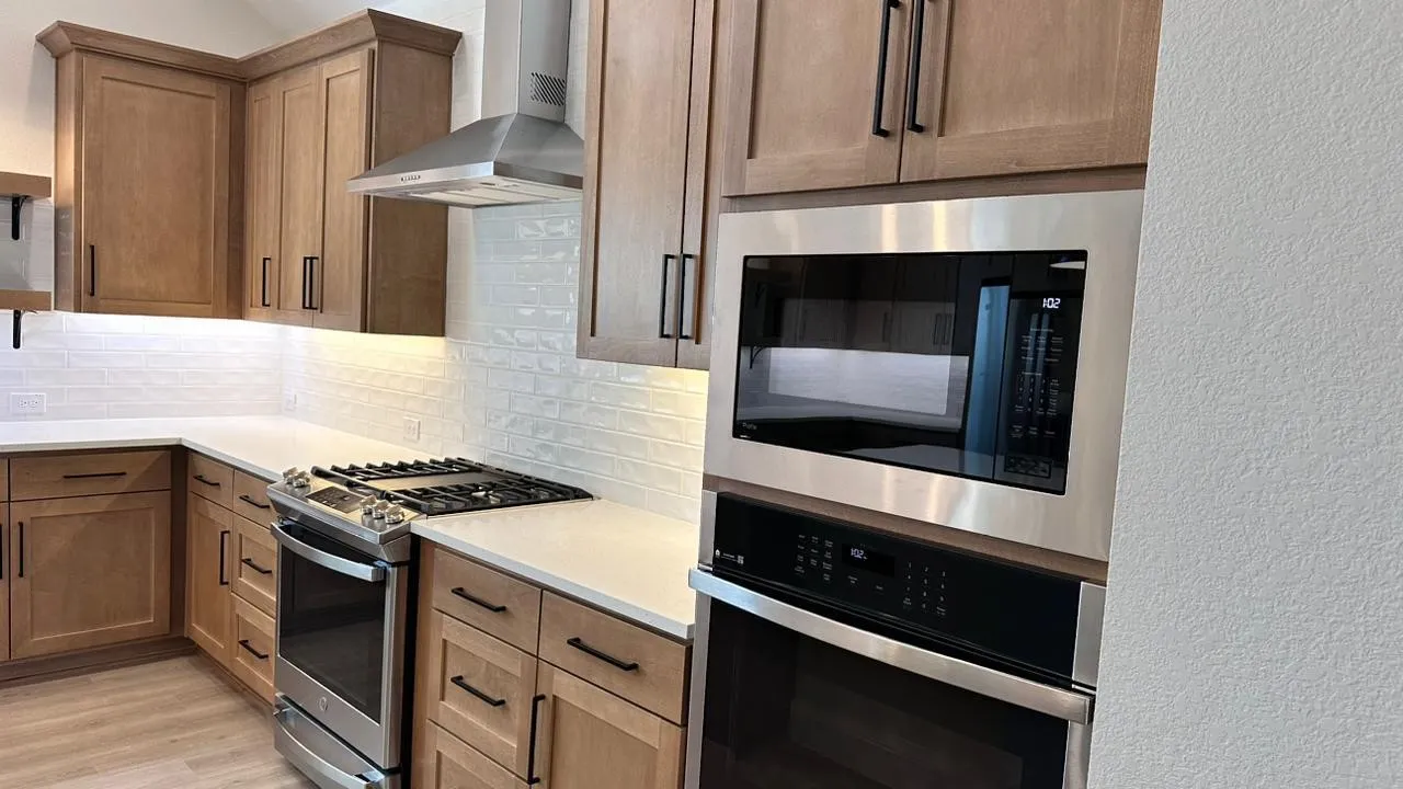 Wood-finish cabinetry with matte black hardware, white subway tile backsplash, stainless steel gas range, stainless steel range hood, and wood-finish flooring