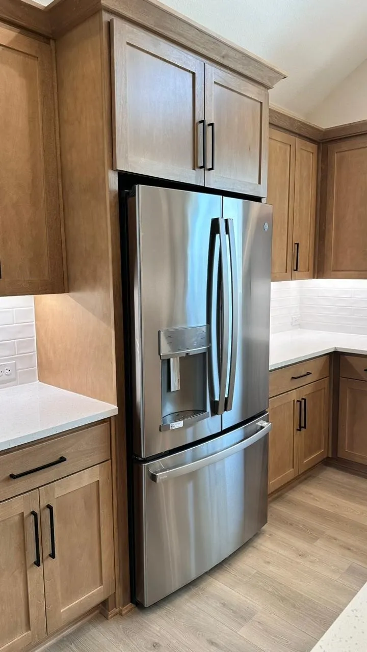 Stainless steel French door refrigerator, light wood-finish cabinetry, white countertops, subway tile backsplash, and light wood-finish flooring