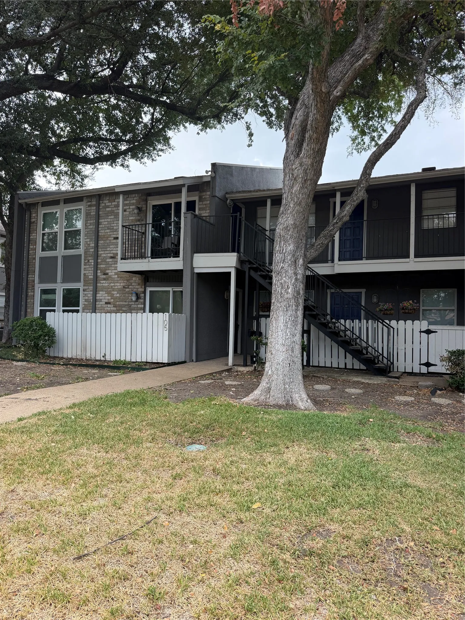 Multi-level exterior featuring brick and panel siding, private balconies, and a white picket fence