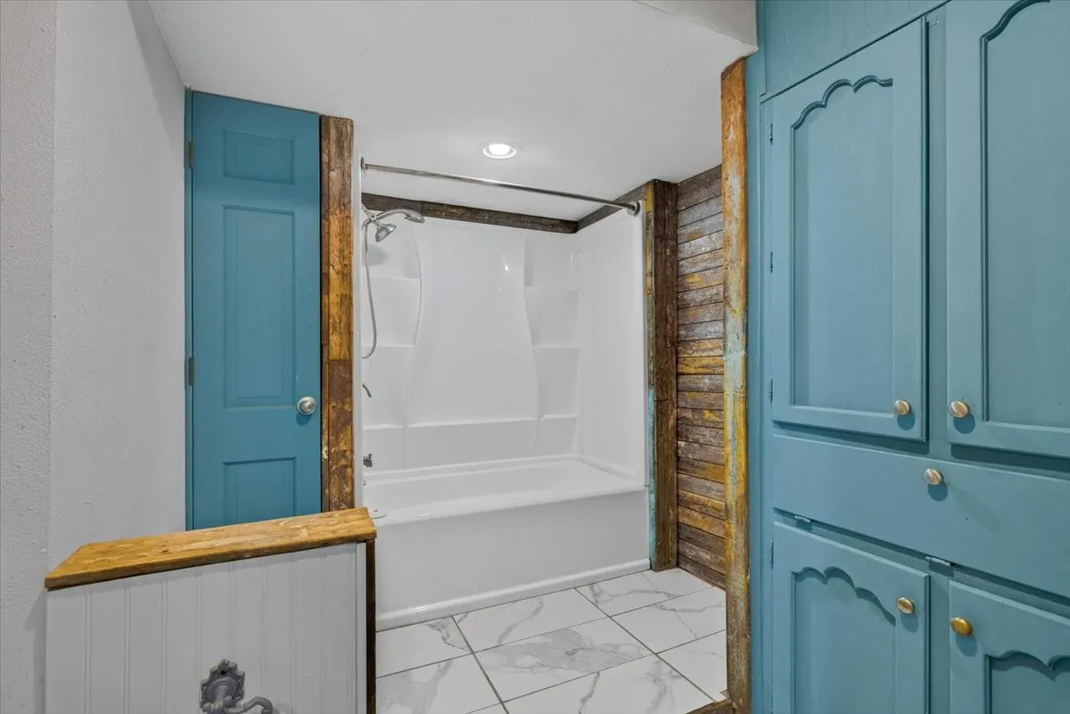 Built-in storage cabinetry with decorative accents, white tile flooring, and a white tub and shower combination