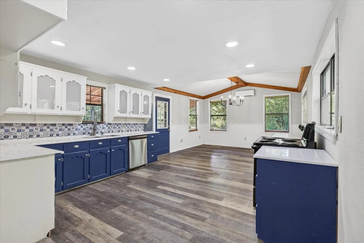 Kitchen featuring white upper cabinetry, blue lower cabinetry, stainless steel dishwasher, and wood-finish flooring