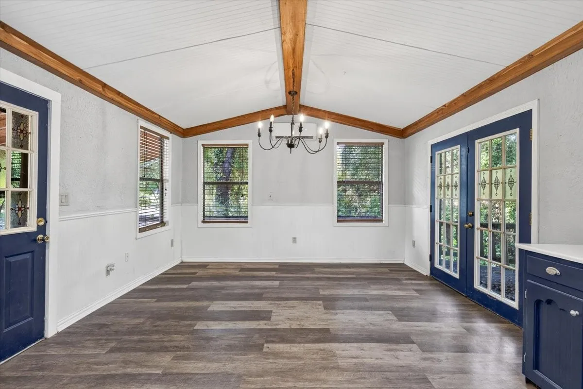 Vaulted ceiling with exposed wood beams, wood-finish flooring, beadboard wainscoting, French doors with decorative lites, and a built-in cabinet with a solid surface countertop