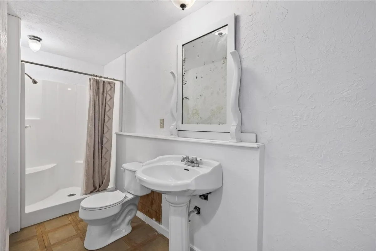 White pedestal sink with chrome-finish faucet, white toilet, and a white shower stall with a chrome-finish shower head