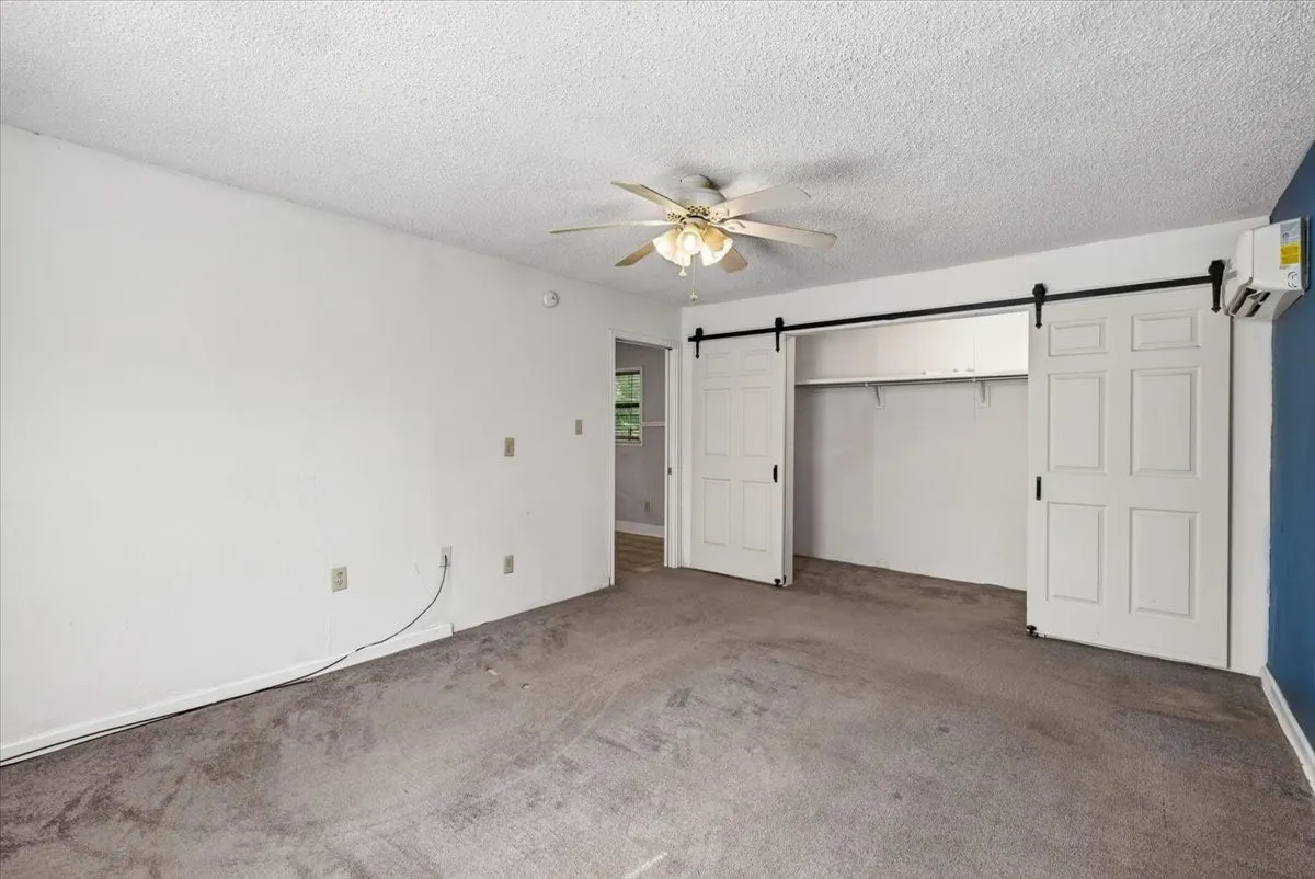 Ceiling fan, barn door style closet, wall-mounted air conditioning unit, white walls, and gray carpeting