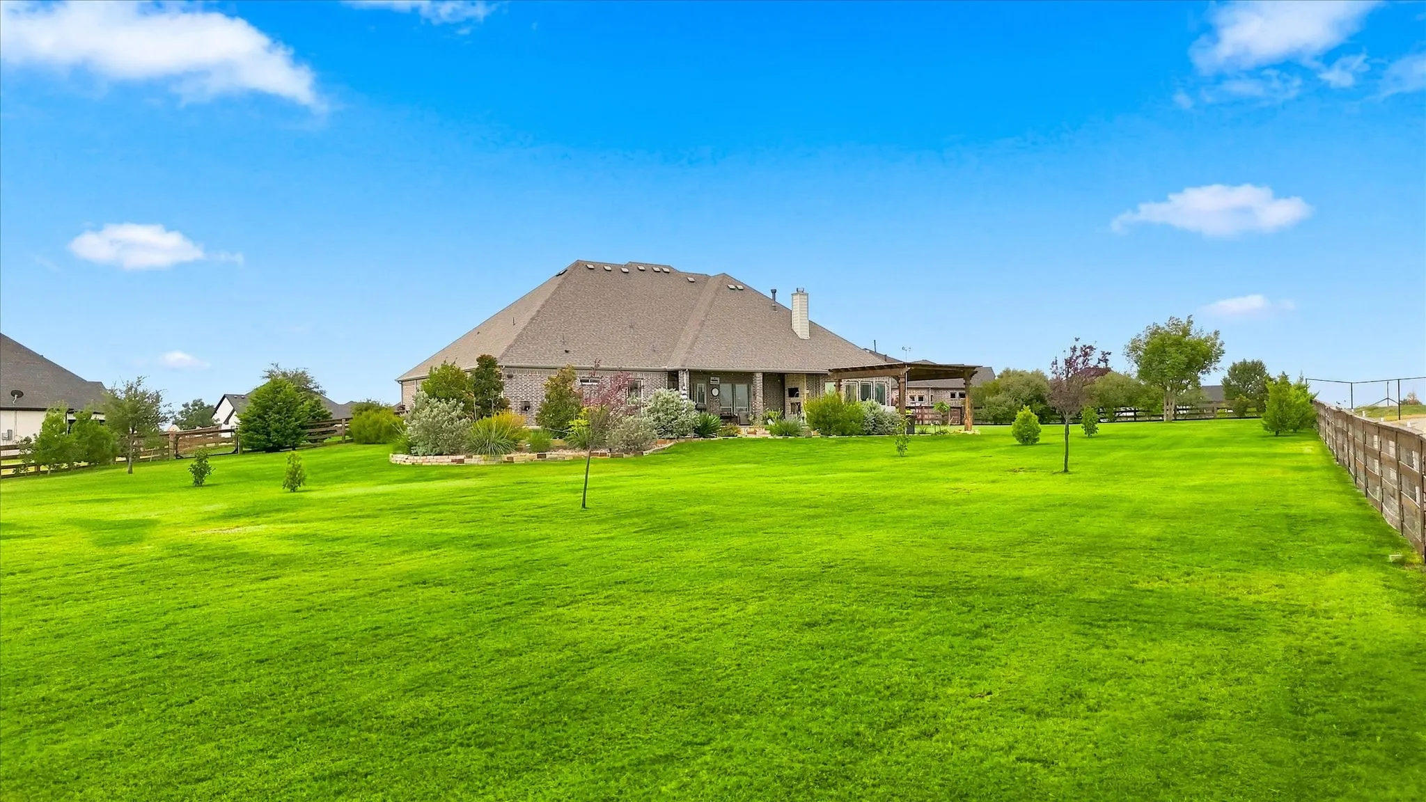 Expansive green space featuring a wood-panel fence, mature landscaping, and a covered back patio