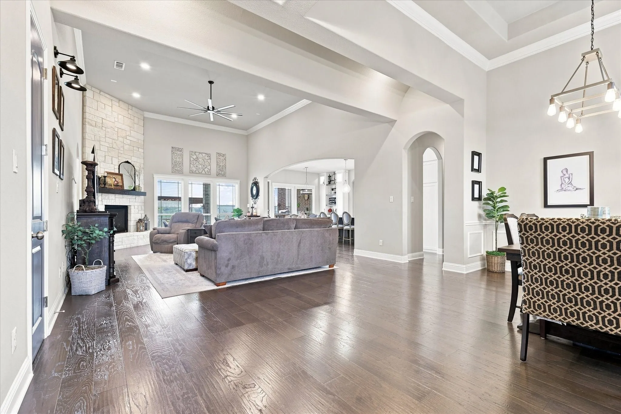Vaulted ceiling with exposed beams, stone-clad fireplace with mantel, polished wood-finish flooring, recessed lighting, and arched doorways