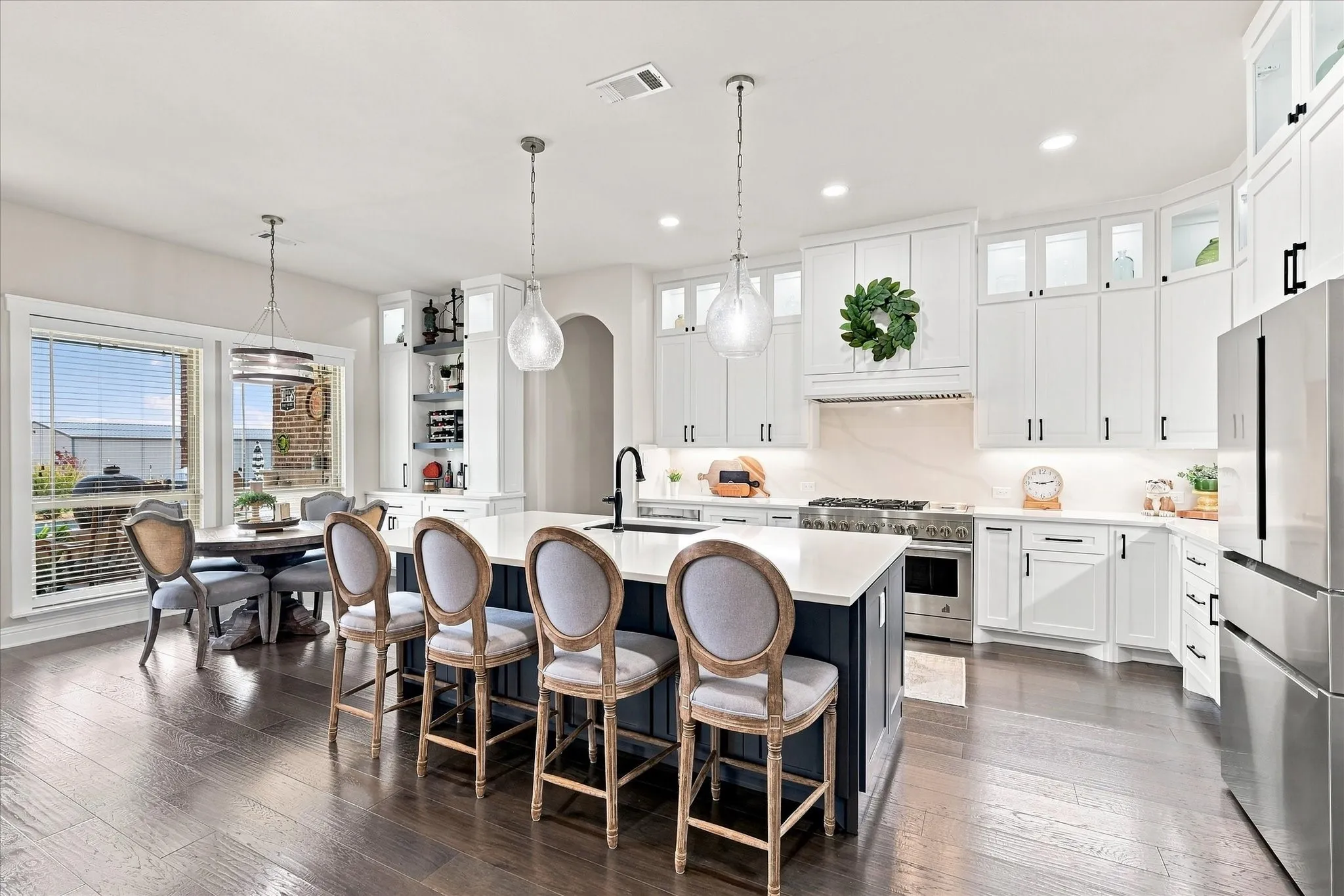 Kitchen featuring an expansive island with seating, white shaker cabinetry, stainless steel appliances, and wood-finish flooring