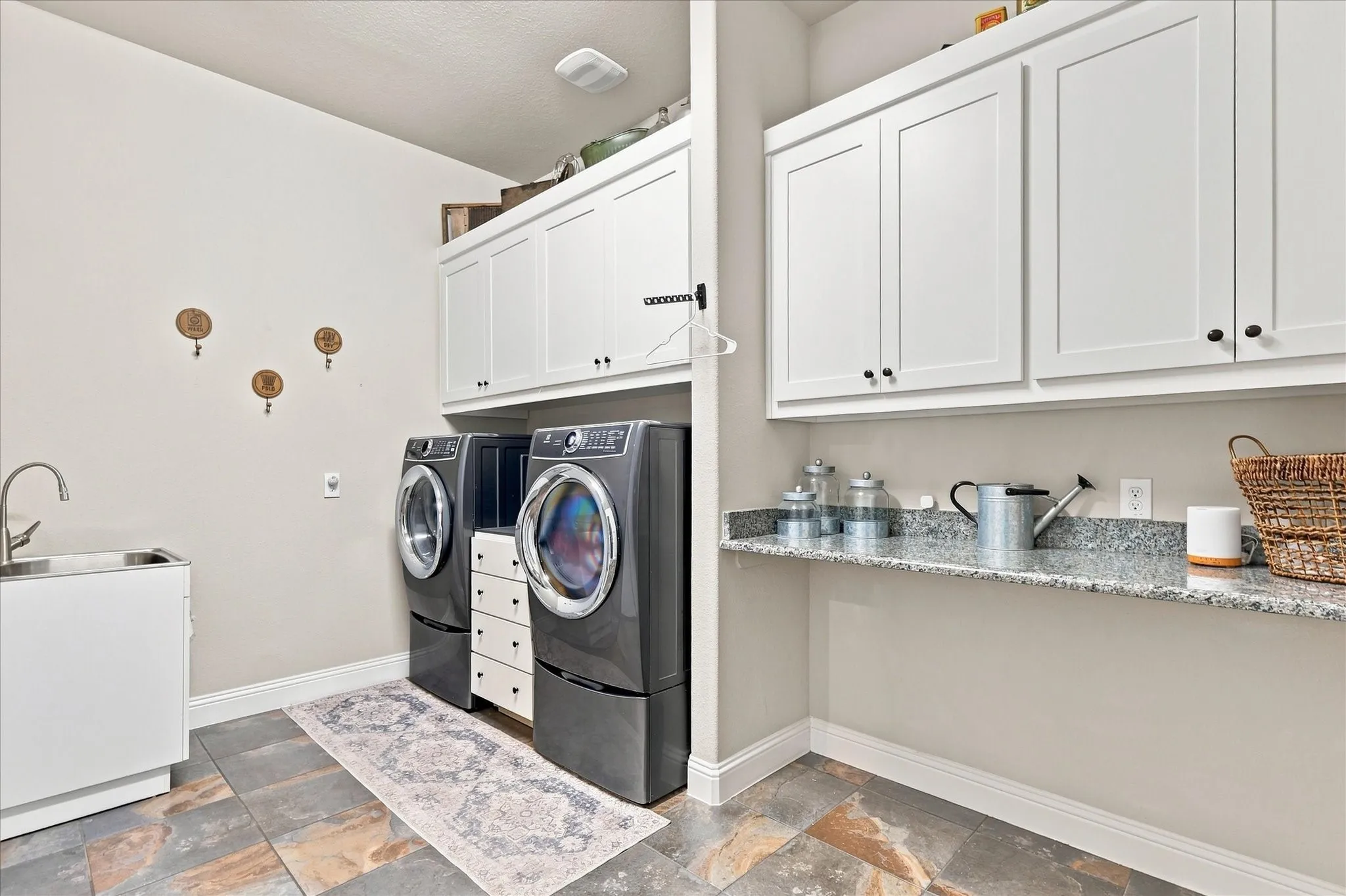 Laundry area featuring extensive white cabinetry, a built-in utility sink, stone-finish flooring, and a stone-finish countertop