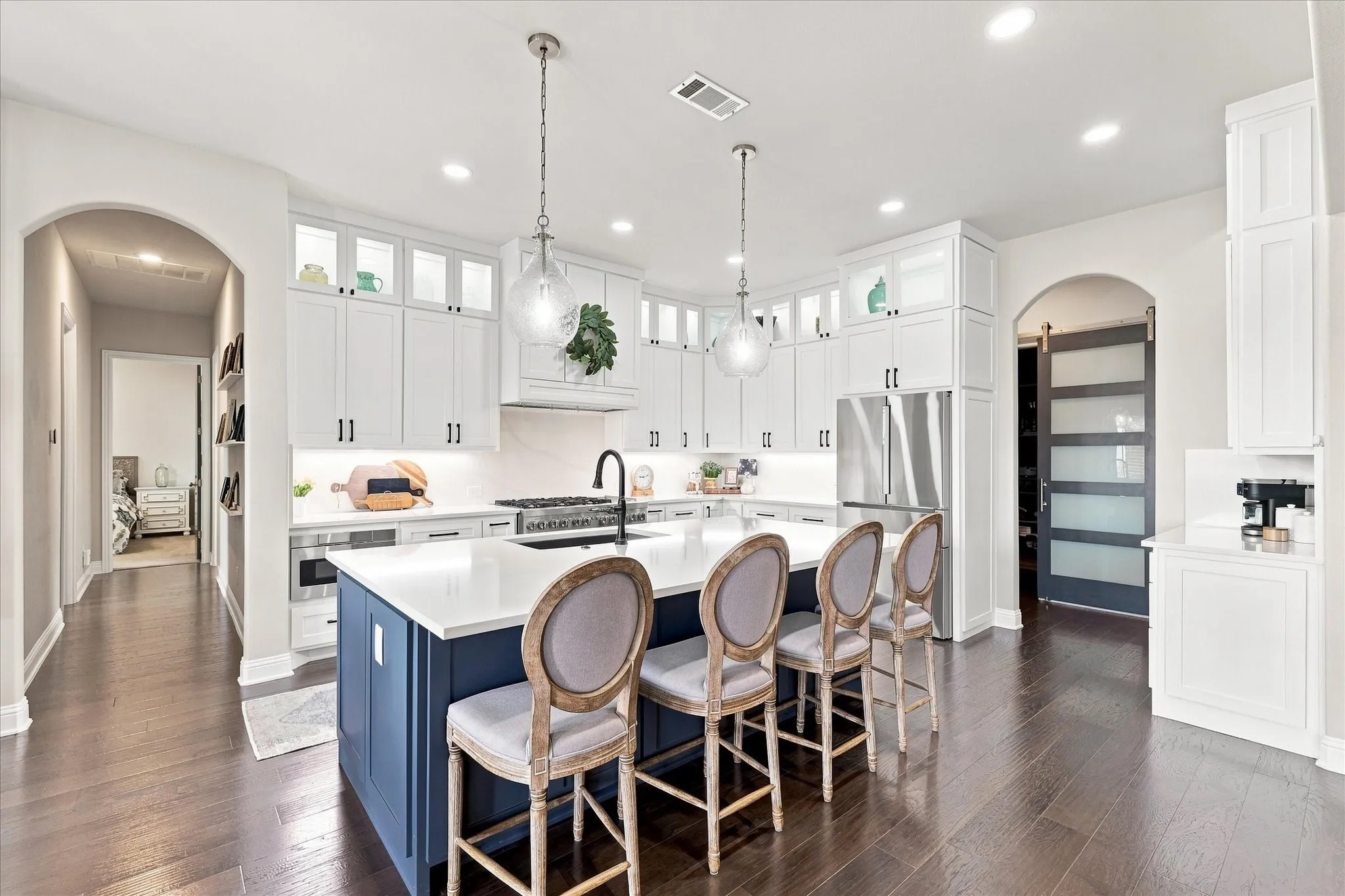 Gourmet kitchen with a large central island, pendant lighting, white cabinetry with upper glass-front accents, stainless steel appliances, and dark wood-finish flooring
