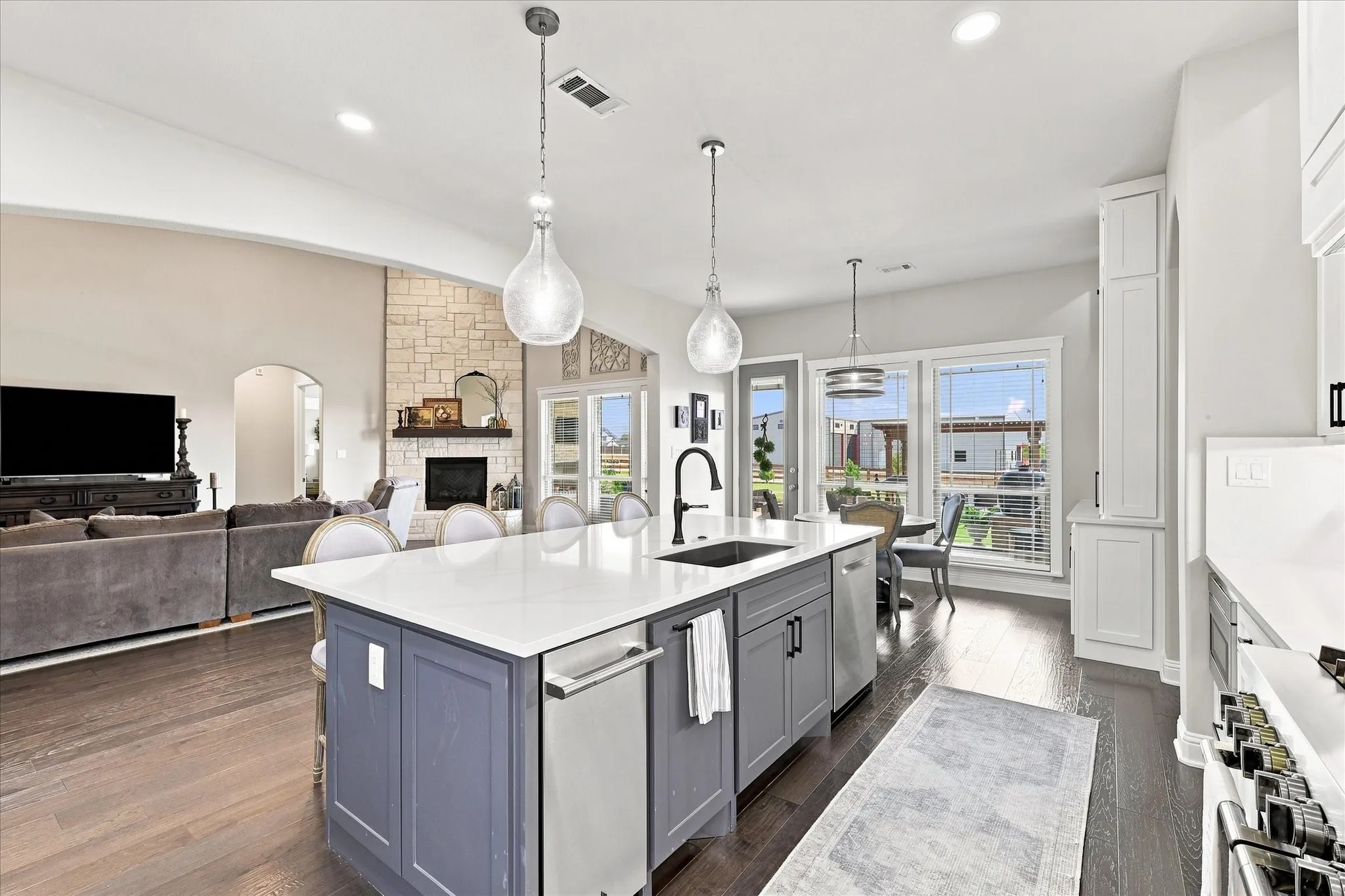 Gourmet kitchen with a large island with dishwasher and ice maker, white countertop, pendant lighting, and dark wood-finish flooring