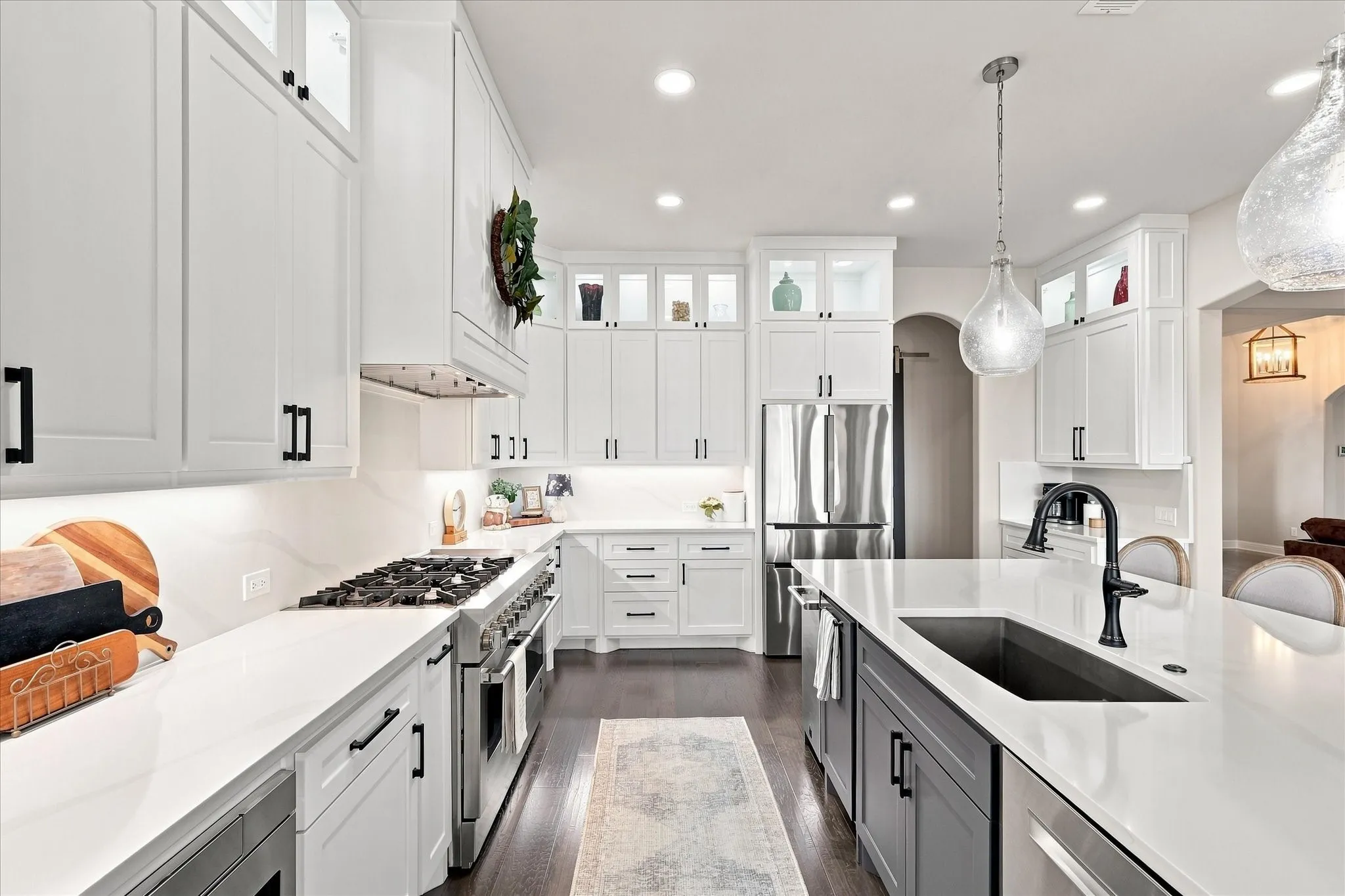 Completely renovated kitchen with white cabinetry, black hardware, stainless steel upgraded appliances, dark wood-finish flooring, recessed lighting, and a kitchen island with an integrated sink